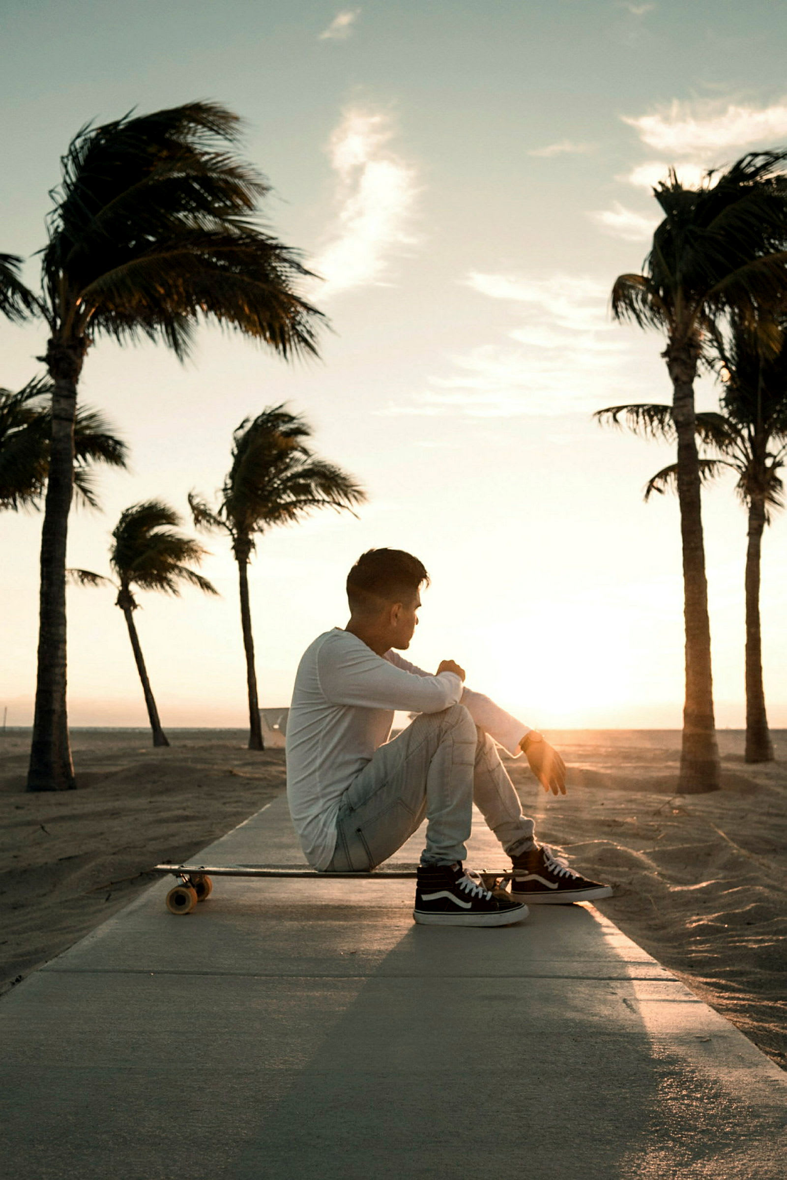 En person sidder på et skateboard ved en strand med palmer i solnedgangen. (AI-genereret tekst)