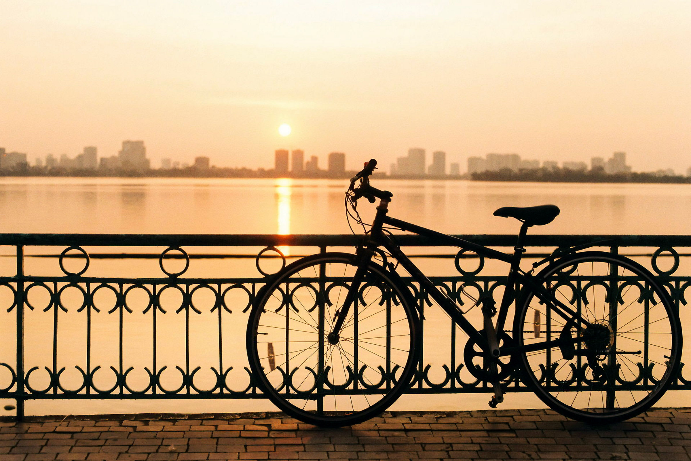En cykel står op ad et smedejernsgelænder ved vandet under en solnedgang. (AI-genereret tekst)