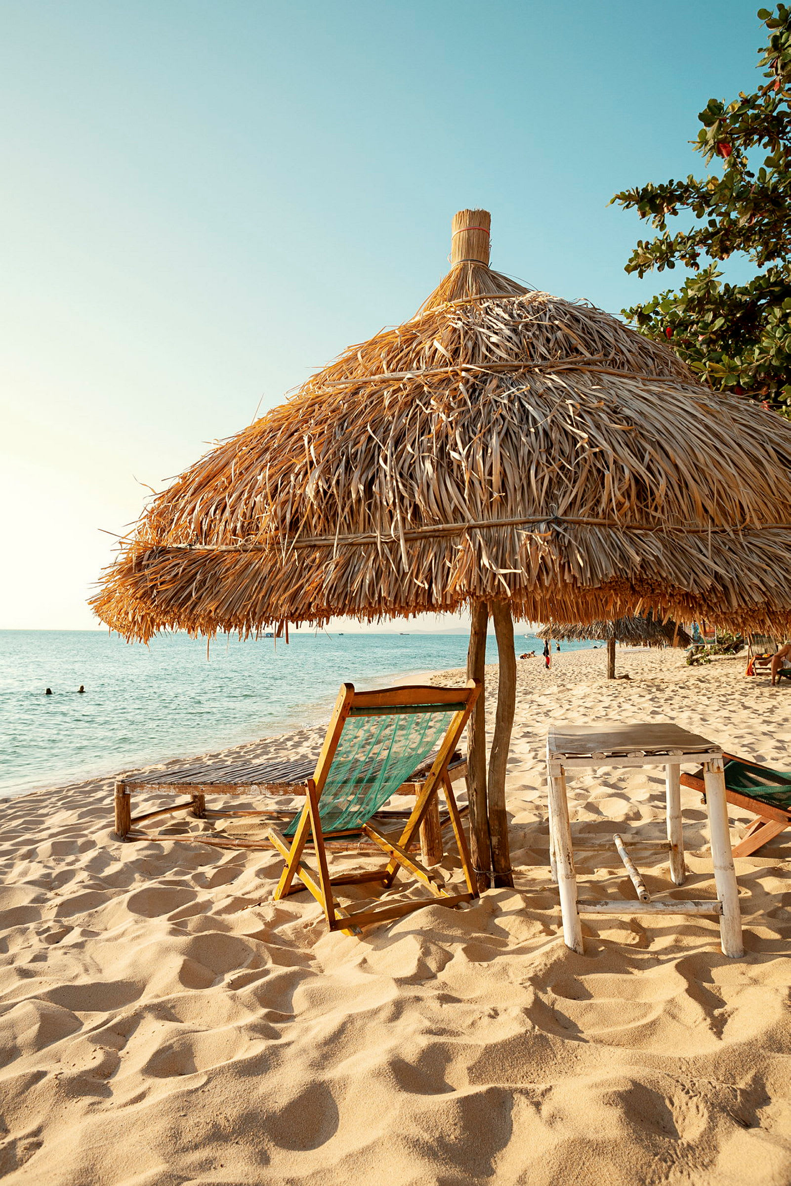 Strand med en liggestol og en parasol lavet af halm står på sandet. (AI-genereret tekst)