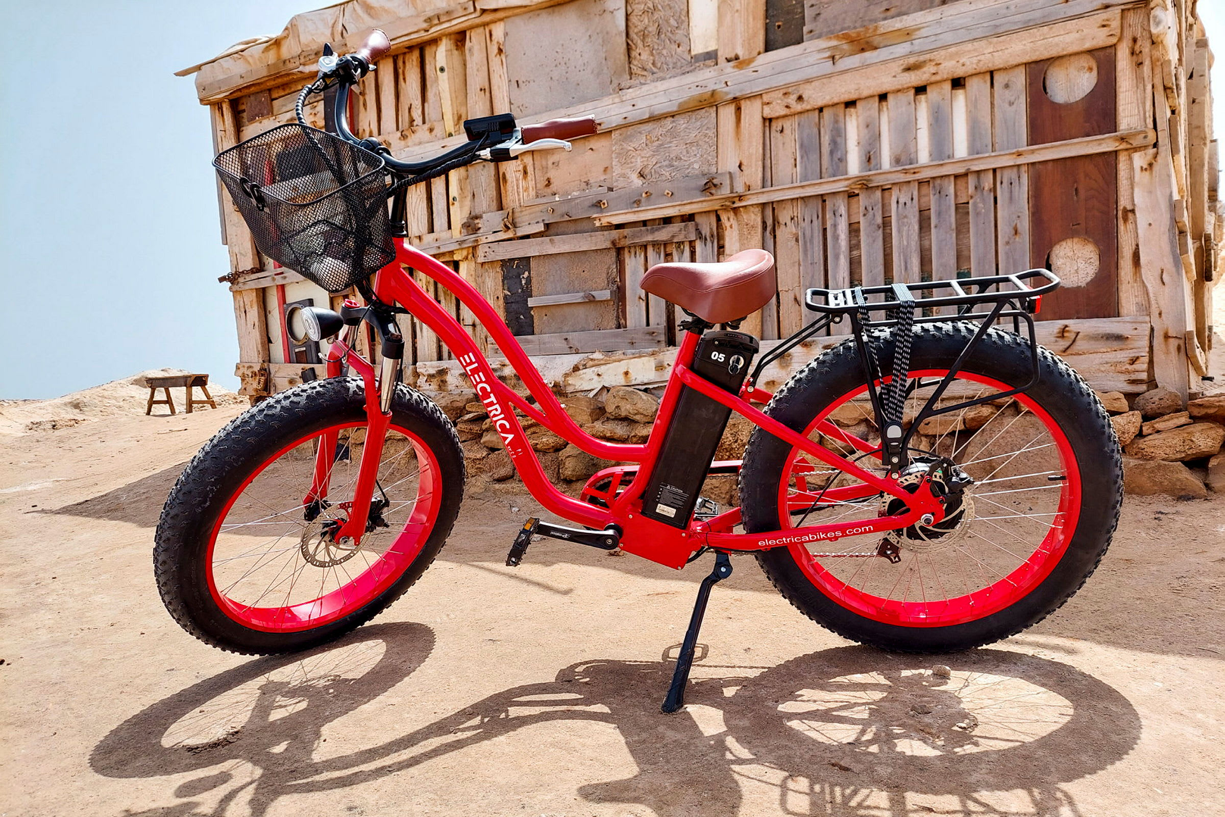 Rød elektrisk cykel står ved siden af en træbygning i et ørkenlandskab. (AI-genereret tekst)