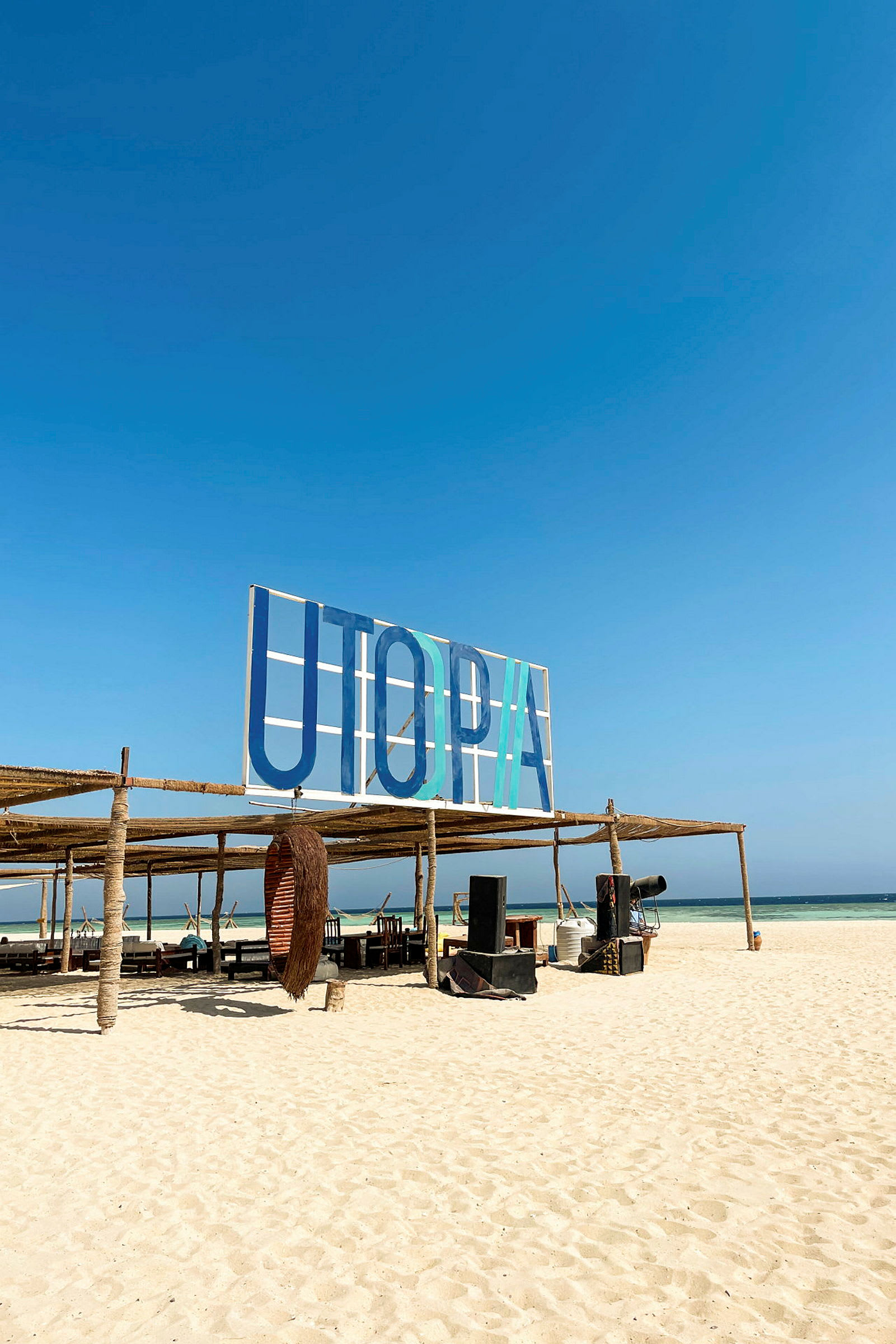 Skilt med teksten 'UTOPIA' på en strand med siddepladser og rekvisitter. (AI-genereret tekst)