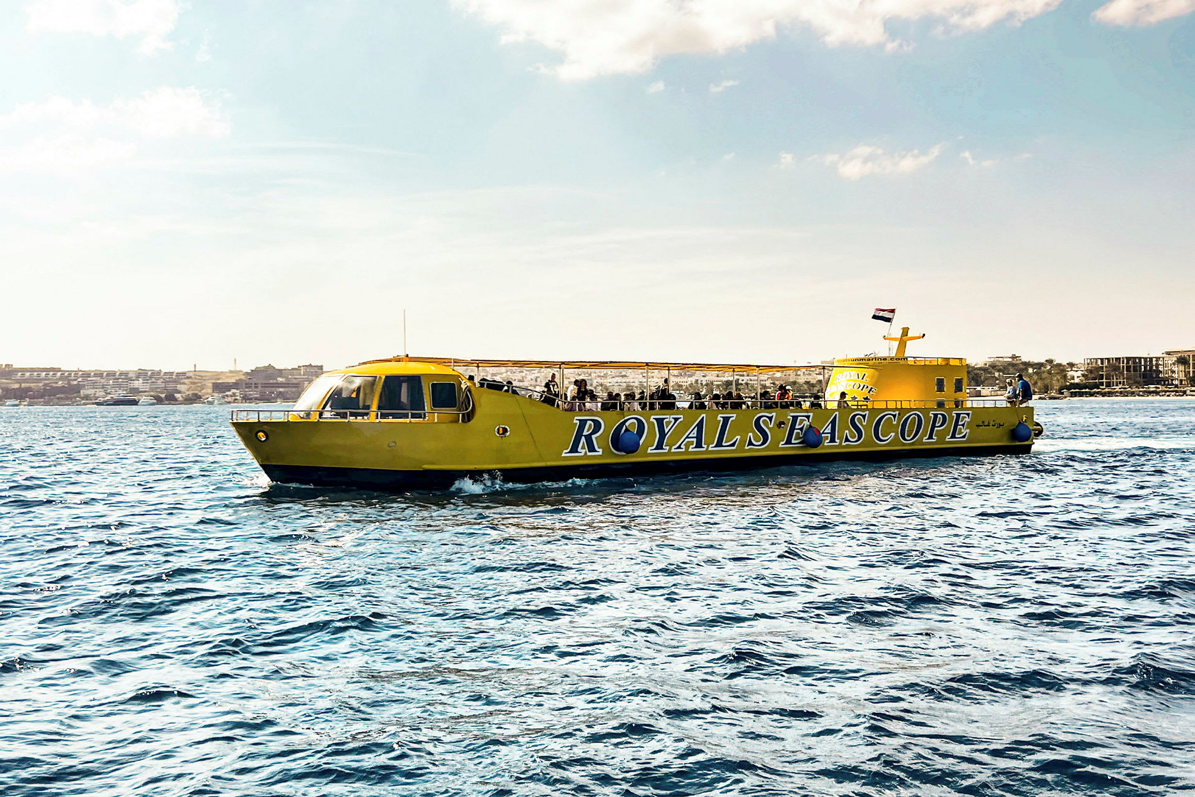 En gul sightseeingbåd med teksten 'ROYALS SEA SCOPE' ses på vandet. (AI-genereret tekst)