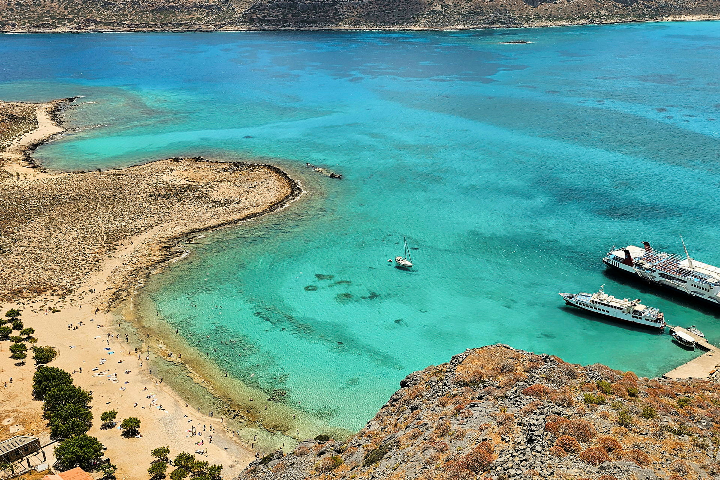 En strand med turkisblåt vand. Der er både i vandet og mennesker på stranden. (AI-genereret tekst)
