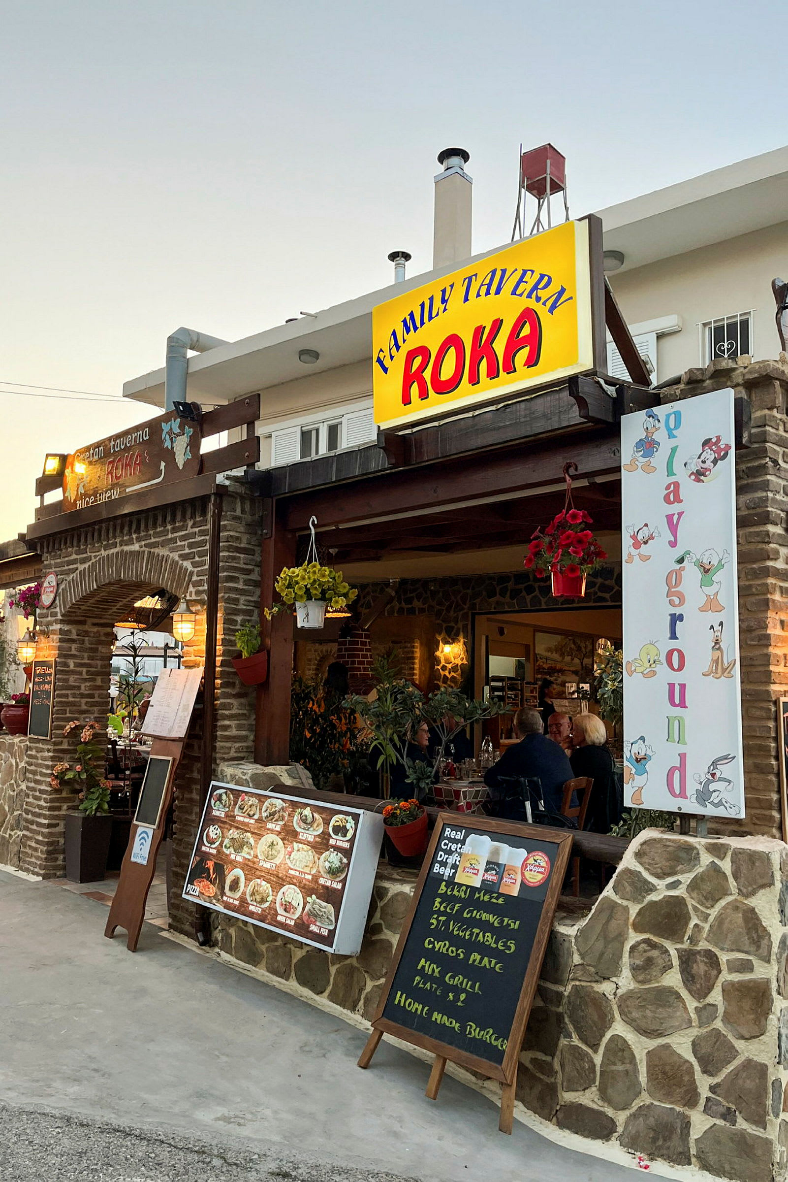 Restaurant med skilte, menuer og dekorationer ved indgangen. Borde og stole kan ses inde. (AI-genereret tekst)