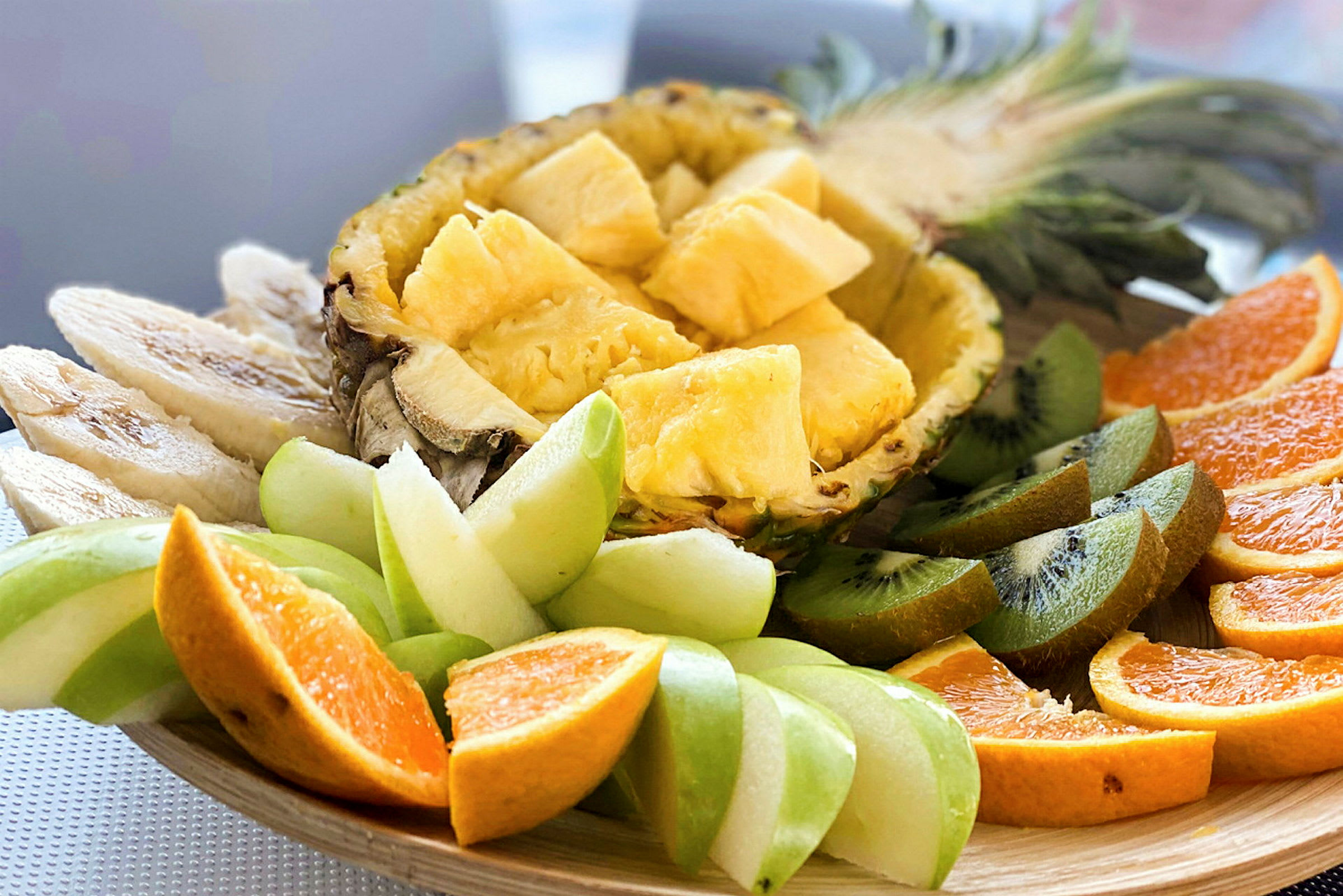 Et fad med forskellige skiveskårne frugter, herunder ananas, kiwi, appelsin og grønne æbler. (AI-genereret tekst)