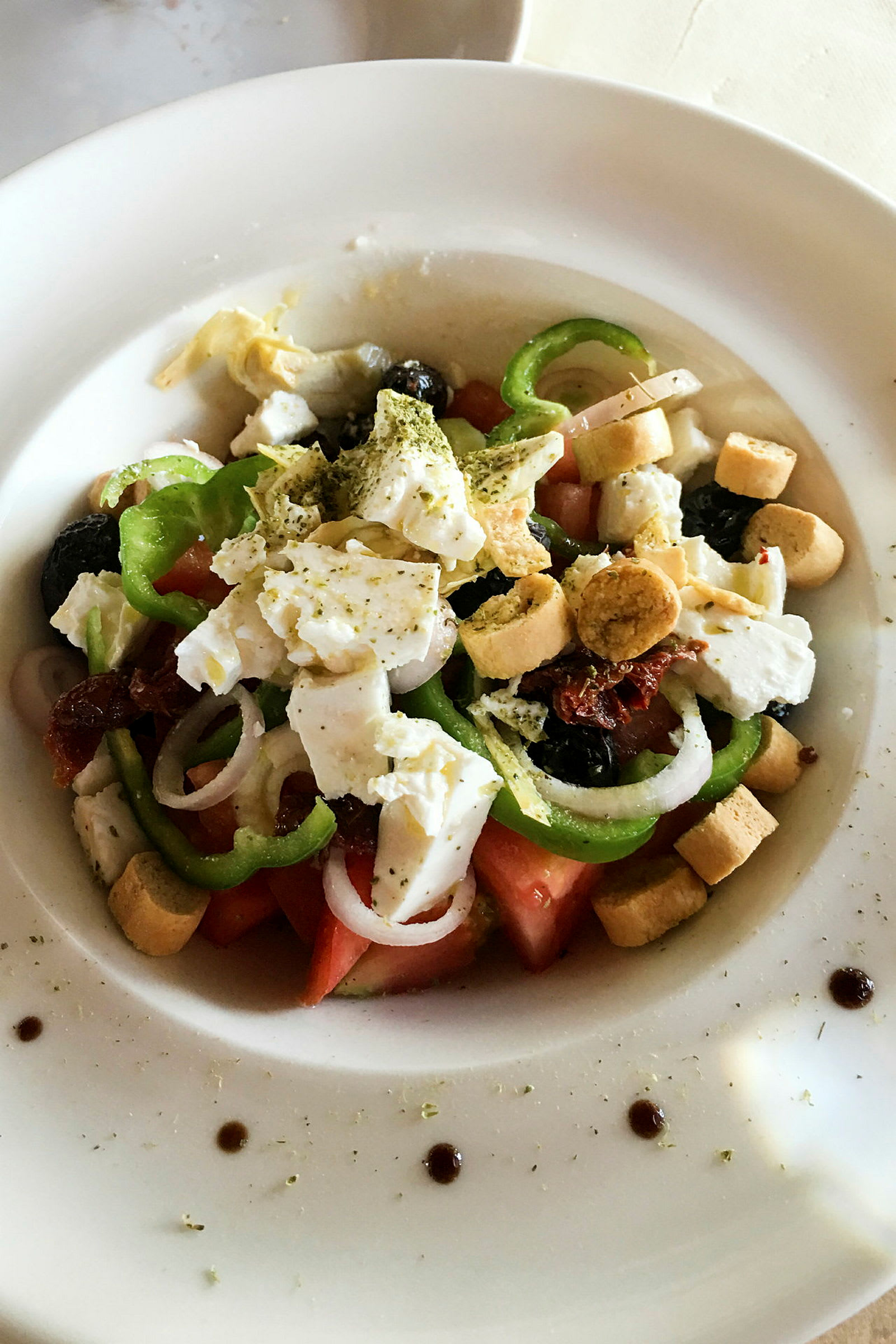 En tallerken med salat, der indeholder tomat, peberfrugt, løg, feta, oliven og krutoner. (AI-genereret tekst)