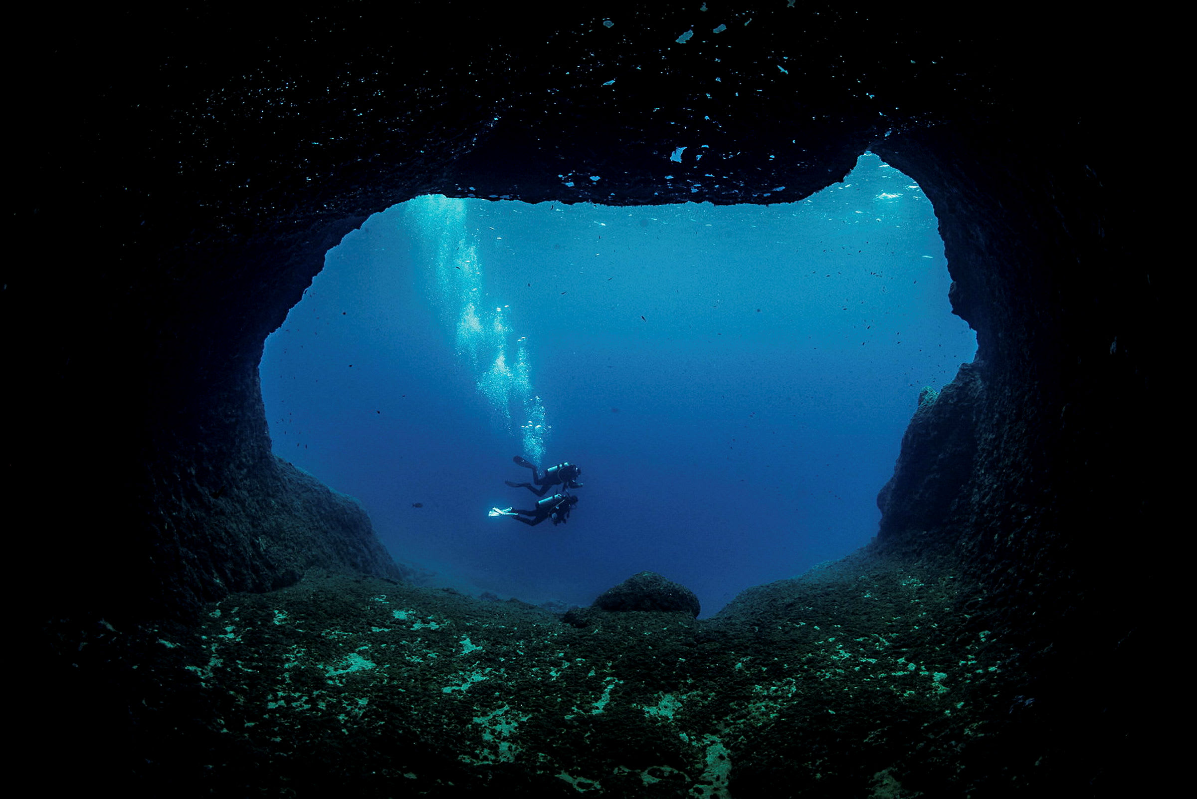 To dykkere svømmer i havet, set fra indersiden af en undervandsgrotte. (AI-genereret tekst)