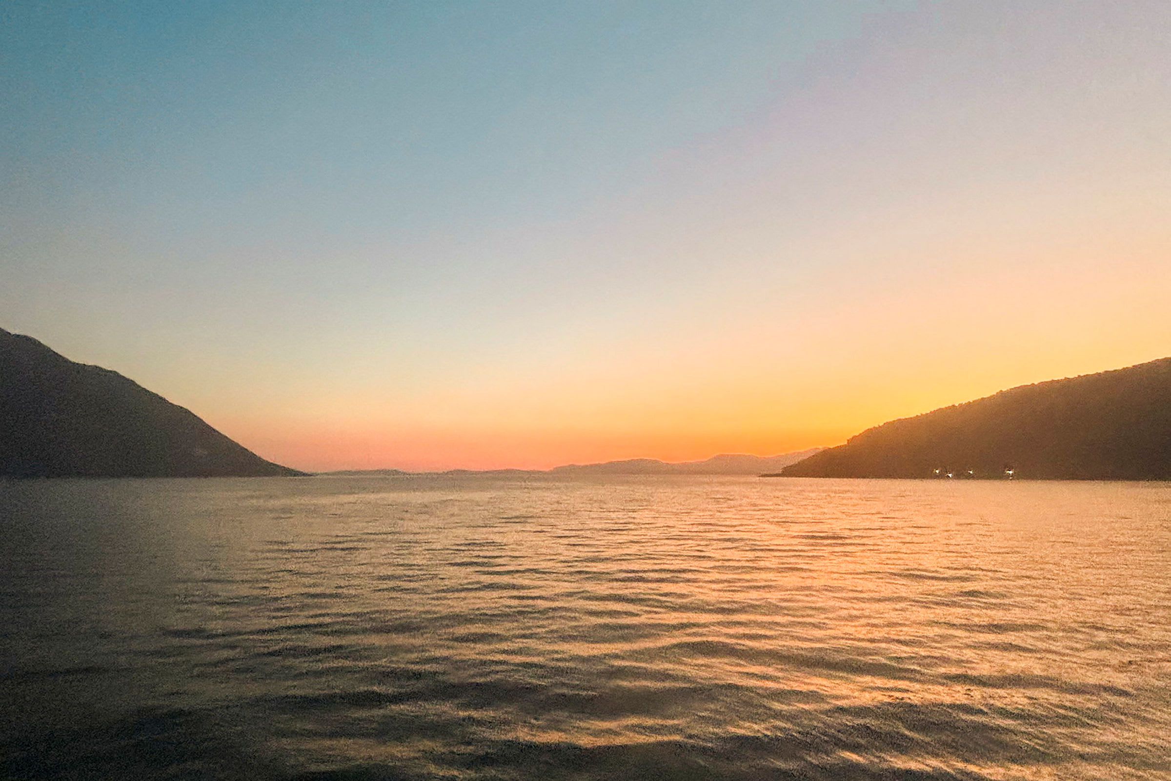 Solnedgang over et roligt hav med bjerge i det fjerne. (AI-genereret tekst)