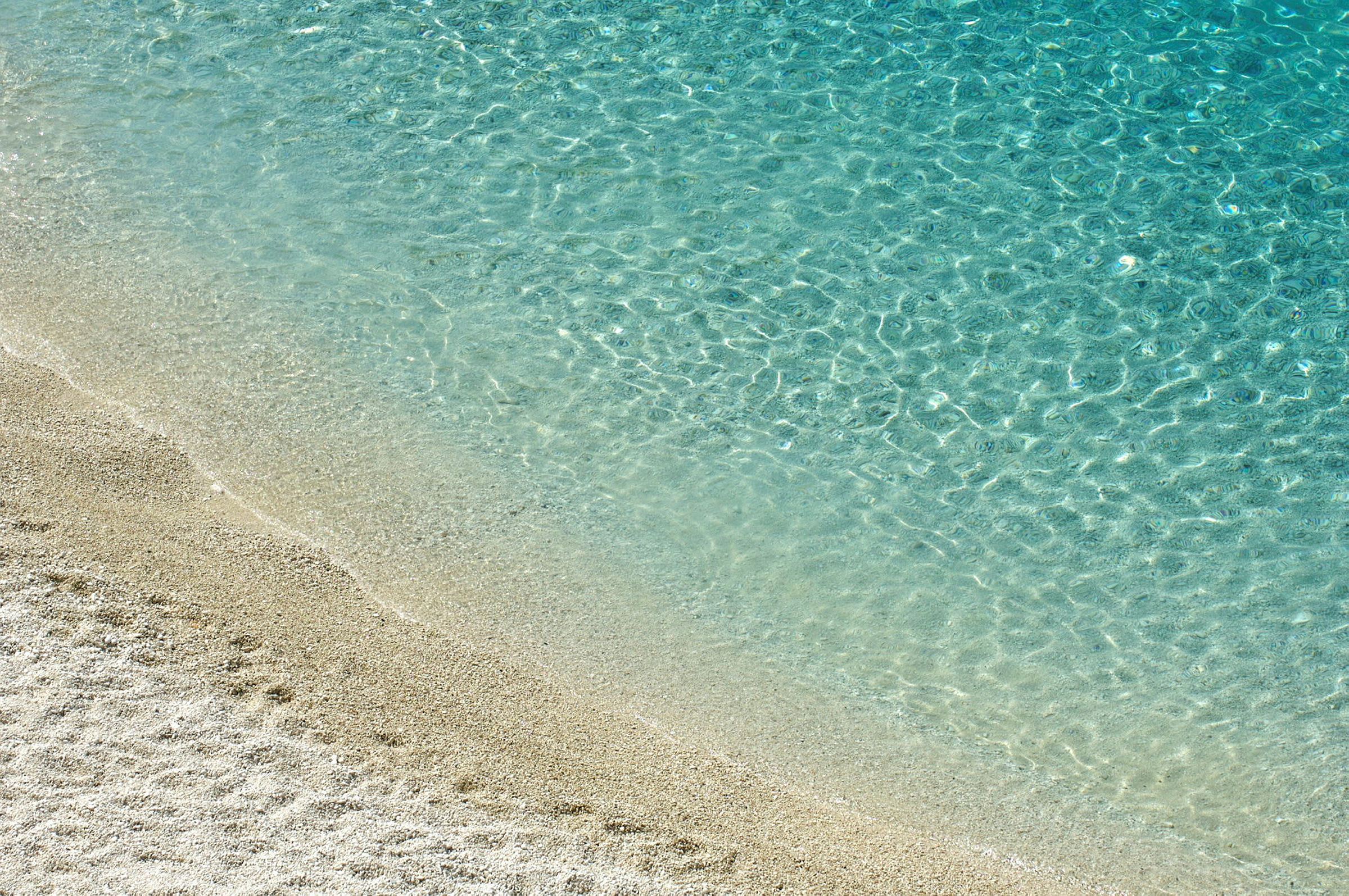Billedet viser et strandområde hvor klart blåt vand møder lyst sand. (AI-genereret tekst)
