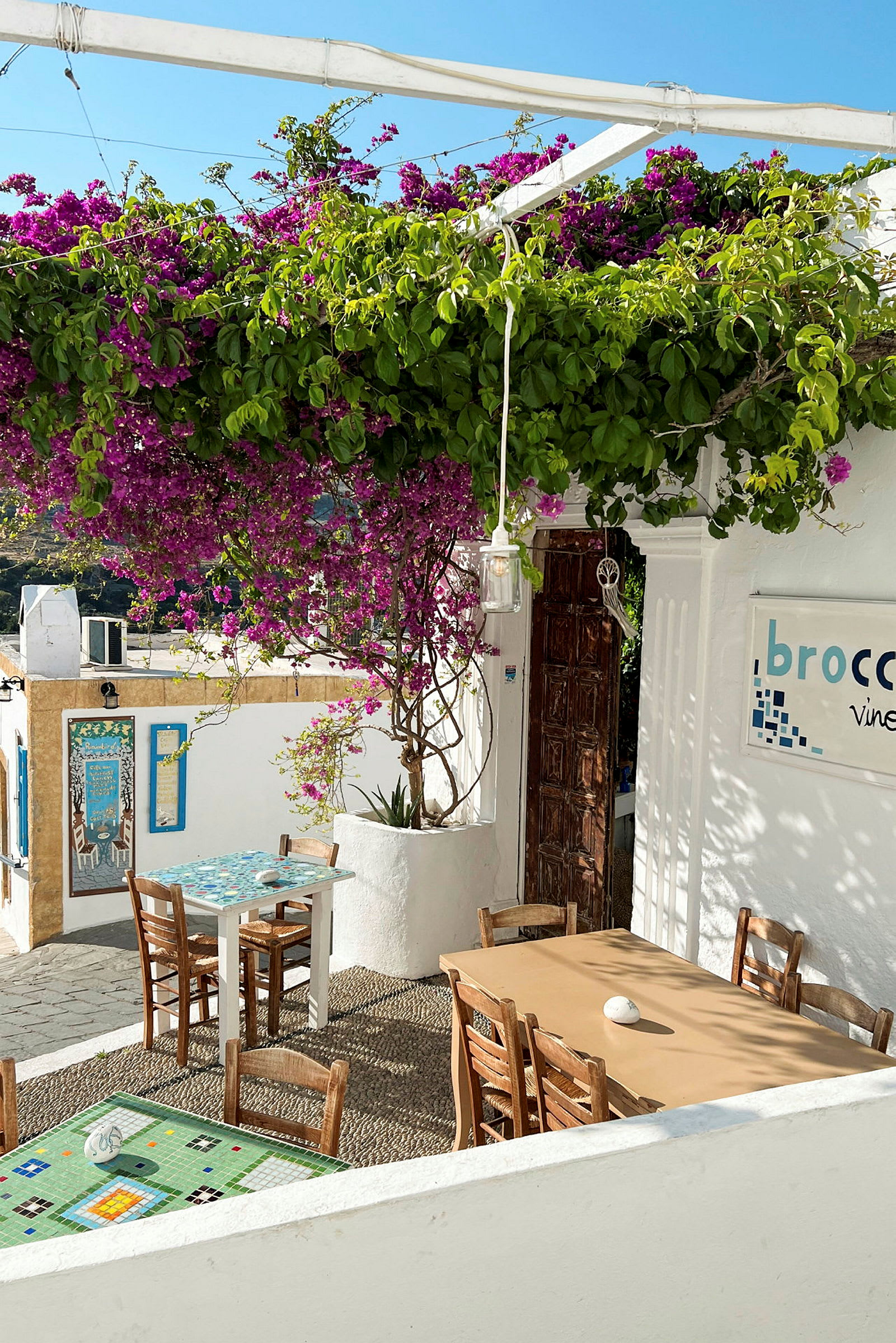 Udendørs område af en restaurant med borde og stole under en blomstrende pergola. (AI-genereret tekst)