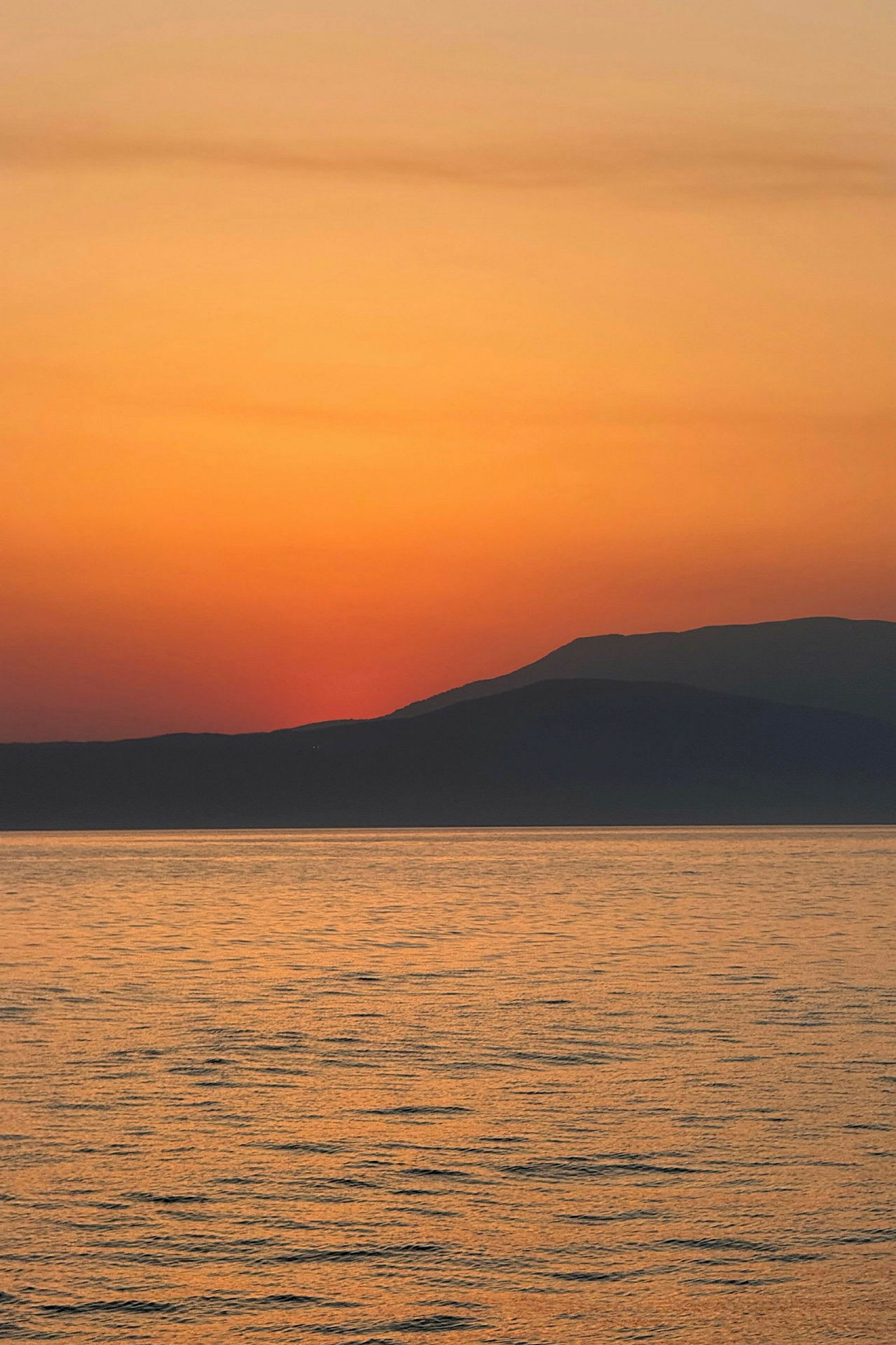 Solnedgang over havet med silhouetter af fjerne bjerge. (AI-genereret tekst)