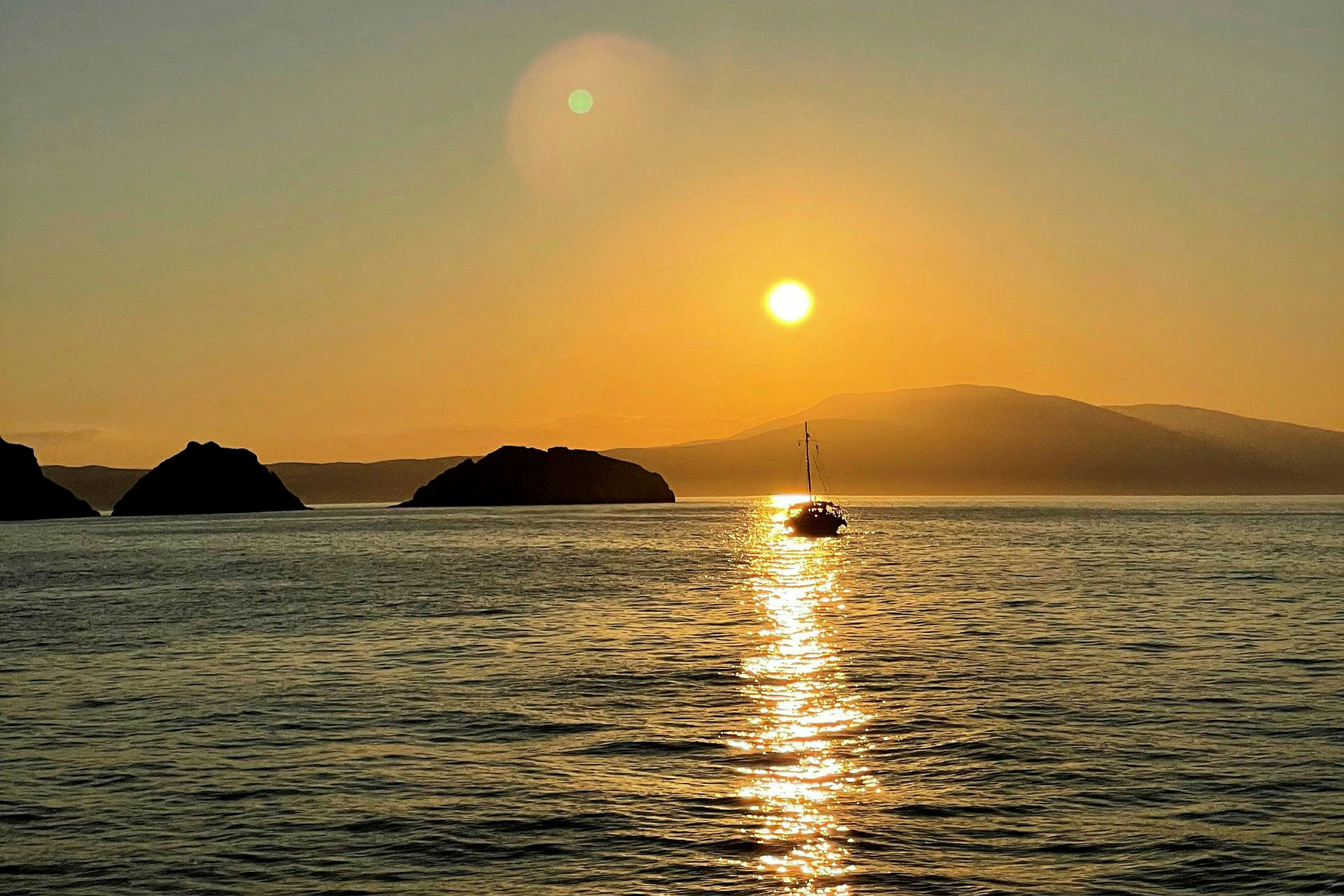 En sejlbåd på havet ved solnedgang, med bjerge i baggrunden. (AI-genereret tekst)