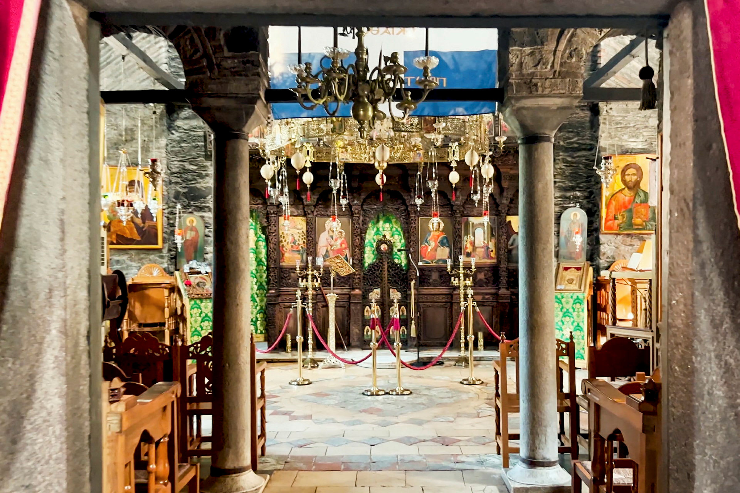 Et interiør af en dekoreret kirke med ikoner og lysekroner. Bænke og søjler fremtrædende. (AI-genereret tekst)