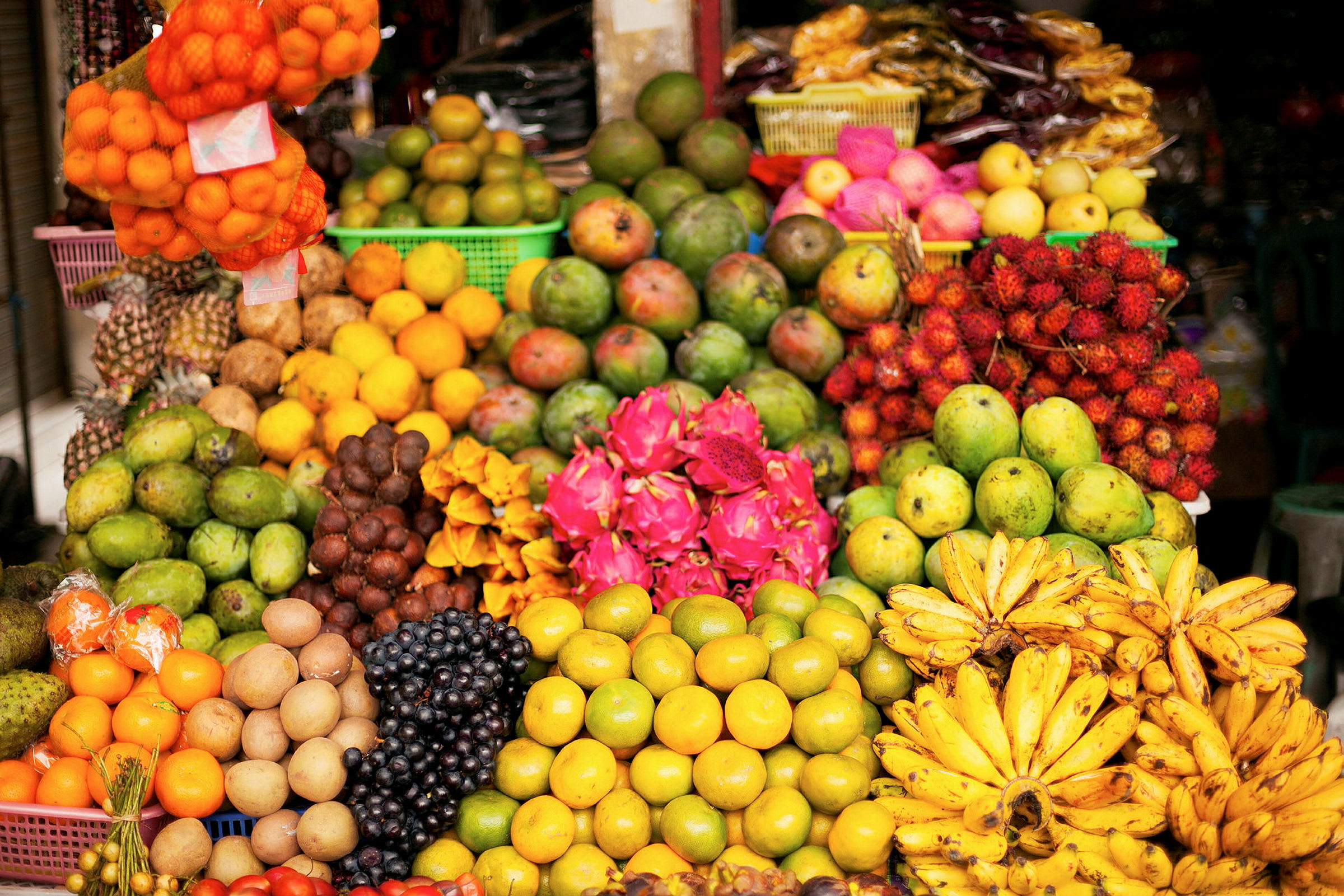 En farverig fremvisning af forskellige frugter som mango, bananer, dragefrugt og andre på et frugtmarked. (AI-genereret tekst)