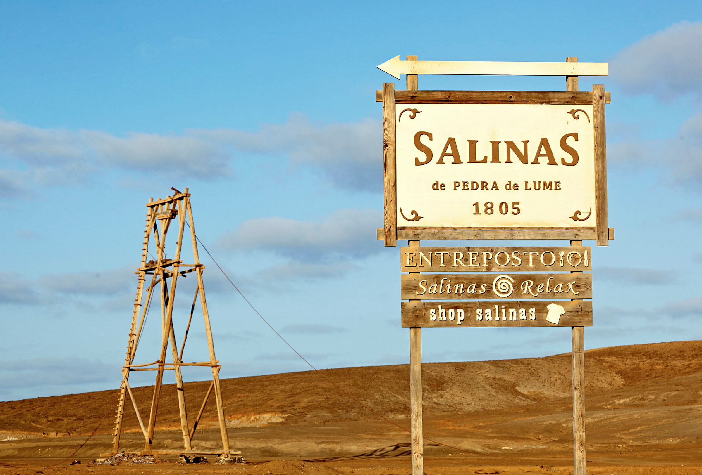 Skilt der markerer Salinas de Pedra de Lume beliggende i et ørkenområde. (AI-genereret tekst)