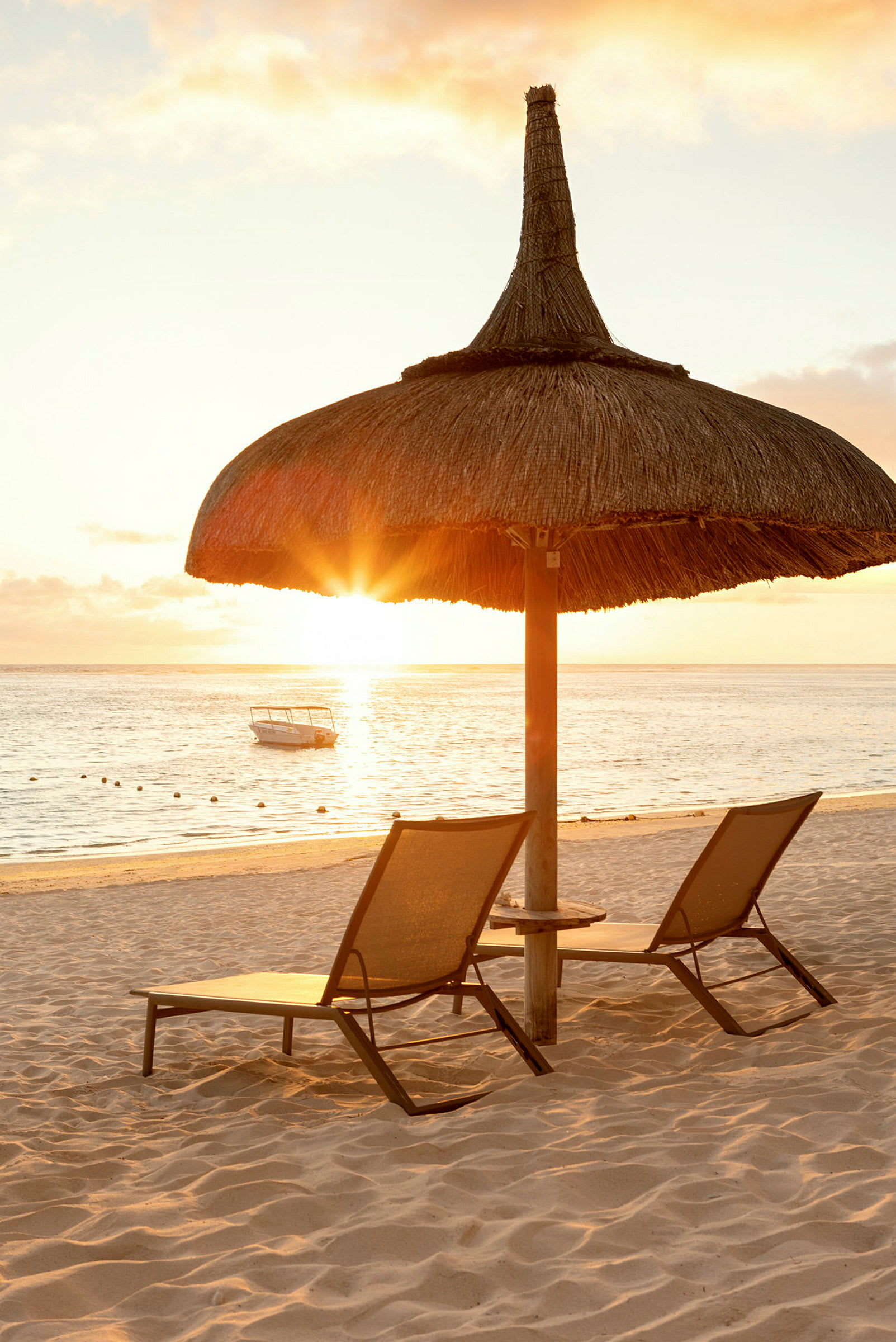 Solnedgang over strand med to solsenge og en parasol lavet af træ og strå. (AI-genereret tekst)