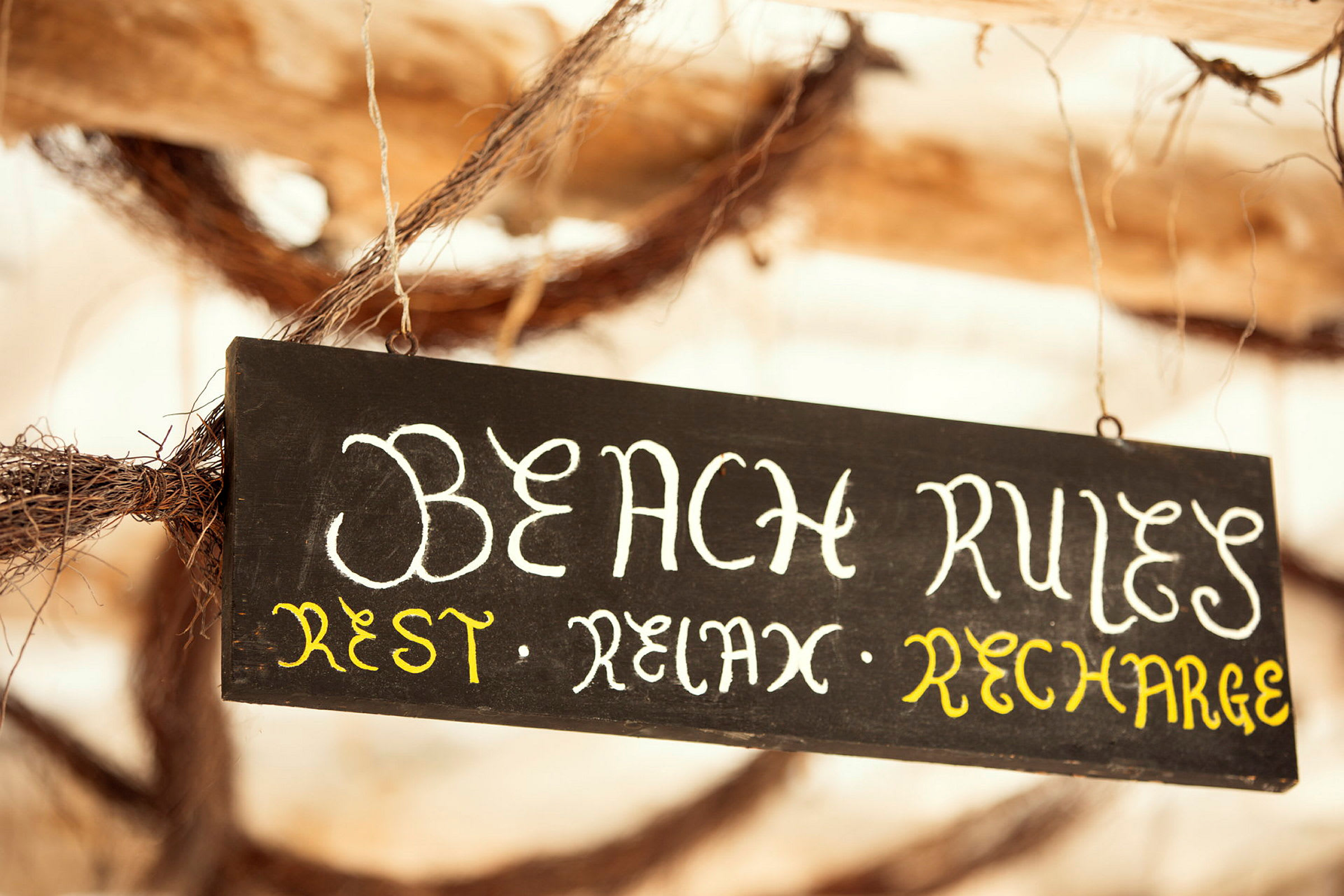 Sort skilt med teksten 'Beach Rules: Rest, Relax, Recharge'. (AI-genereret tekst)