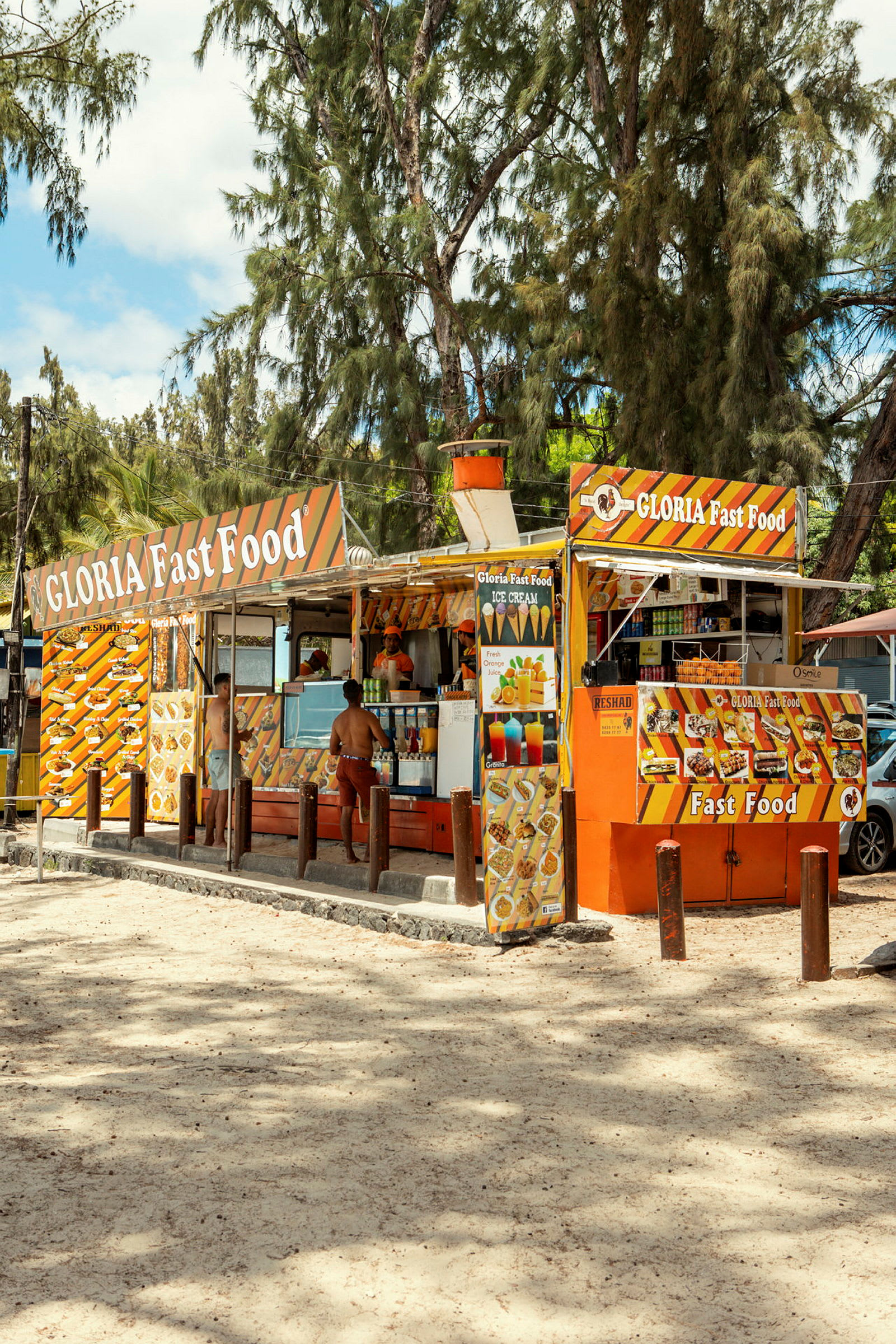 En fastfood-kiosk med orange og gule dekorative skilte, omgivet af træer. (AI-genereret tekst)