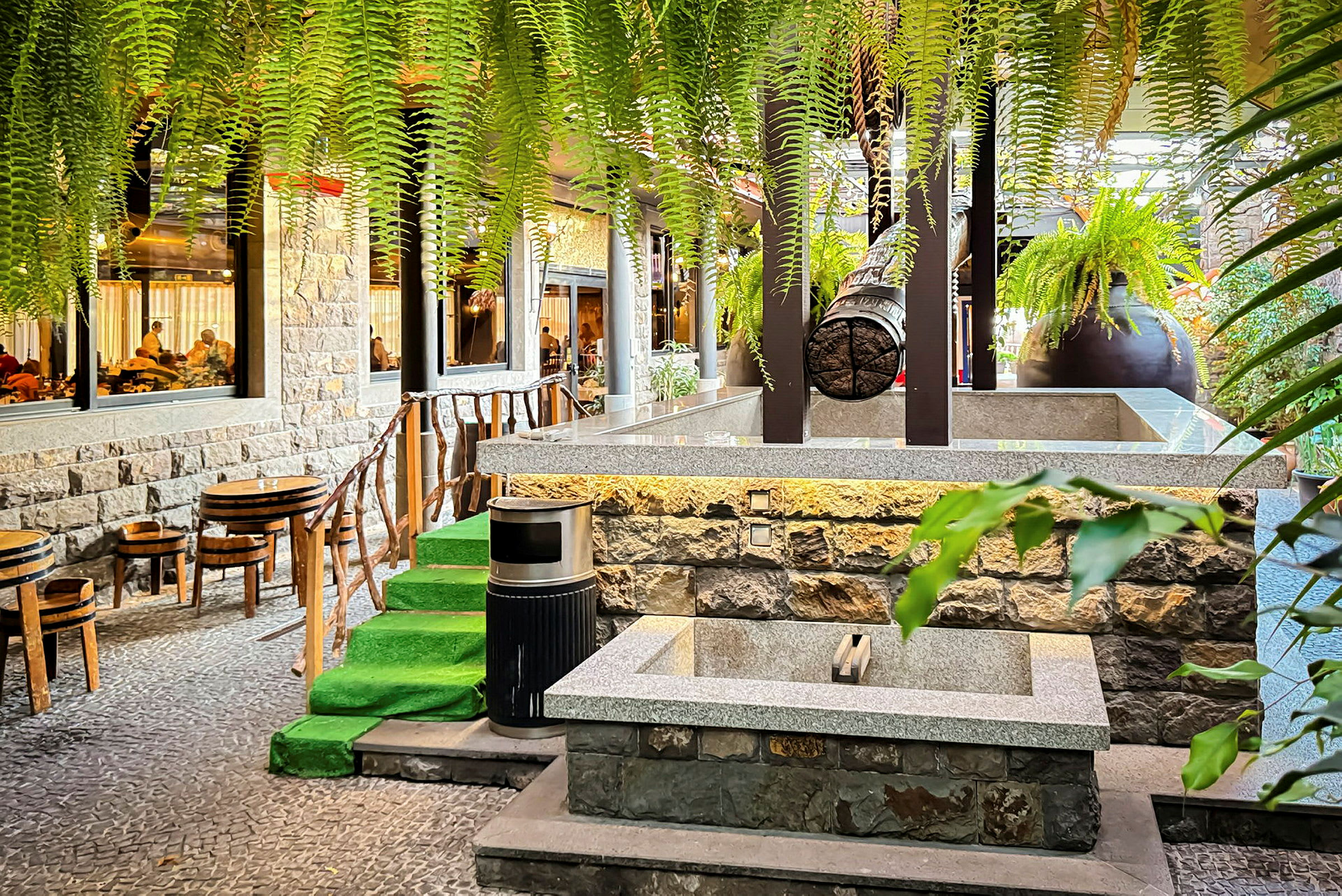Et billede, der viser et udendørsmiljø ved en restaurant med stole, borde, grønne planter og stentrappe. (AI-genereret tekst)