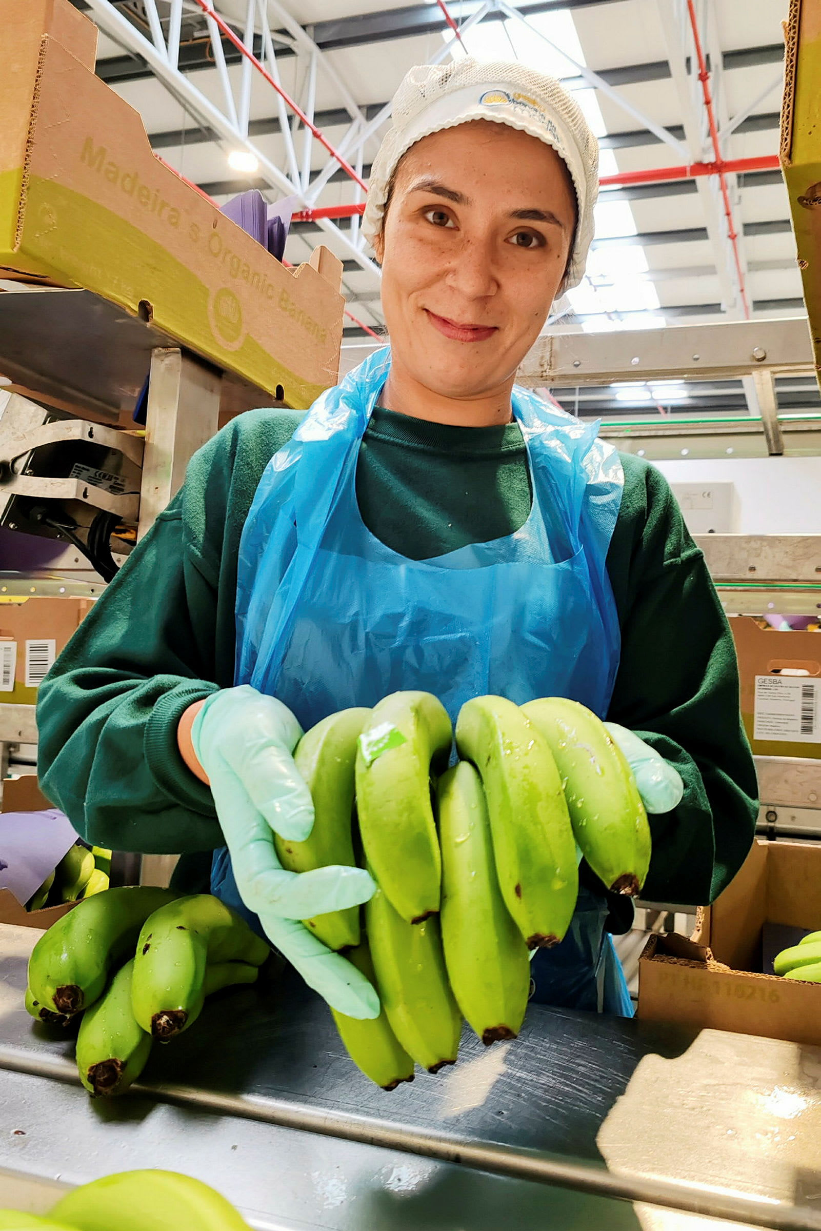 Person løfter grønne bananer, omgivet af kasser og industrielt udstyr. (AI-genereret tekst)