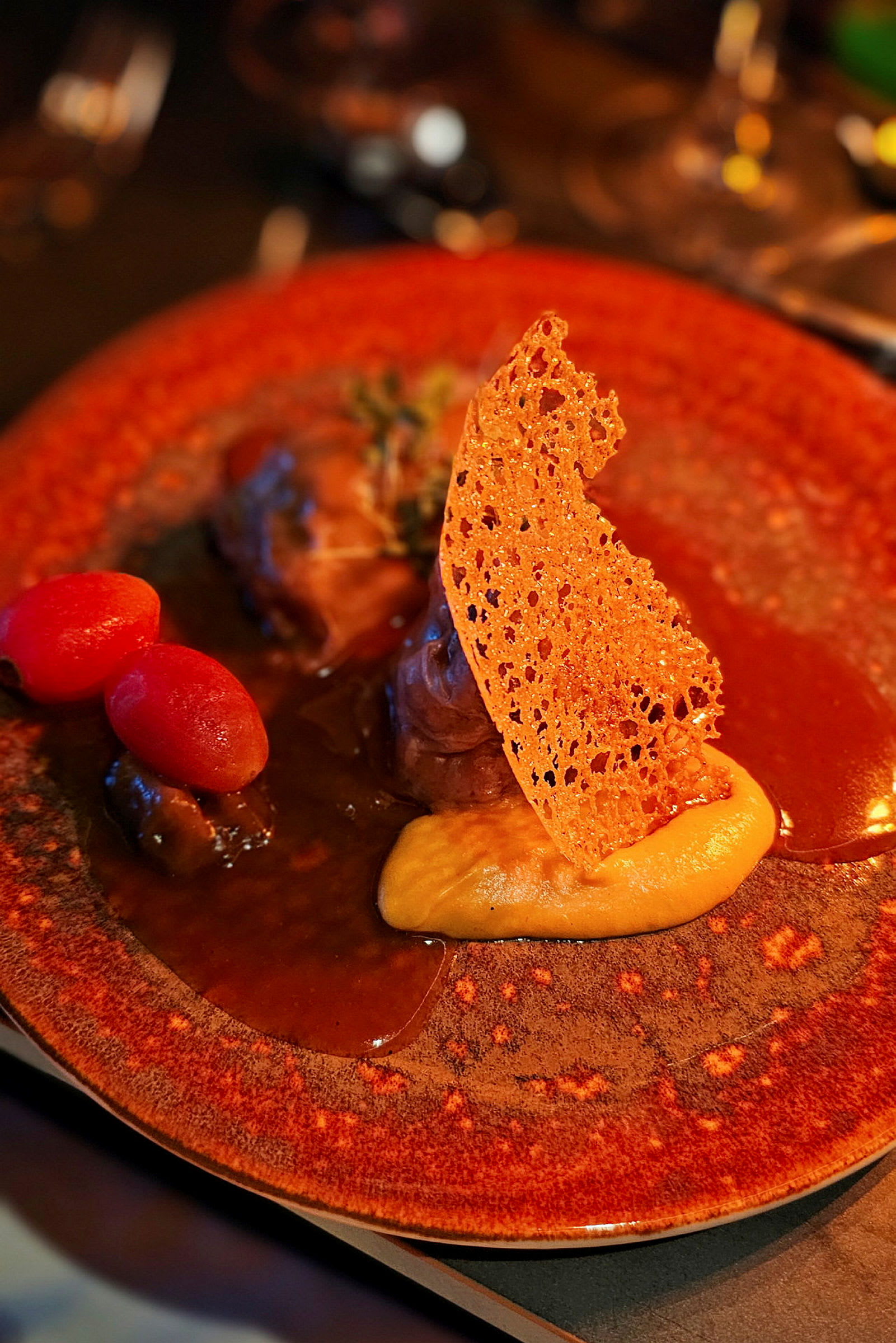 En tallerken med et gourmetmåltid anrettet med sauce, puré, en sprød dekoration og små tomater. (AI-genereret tekst)
