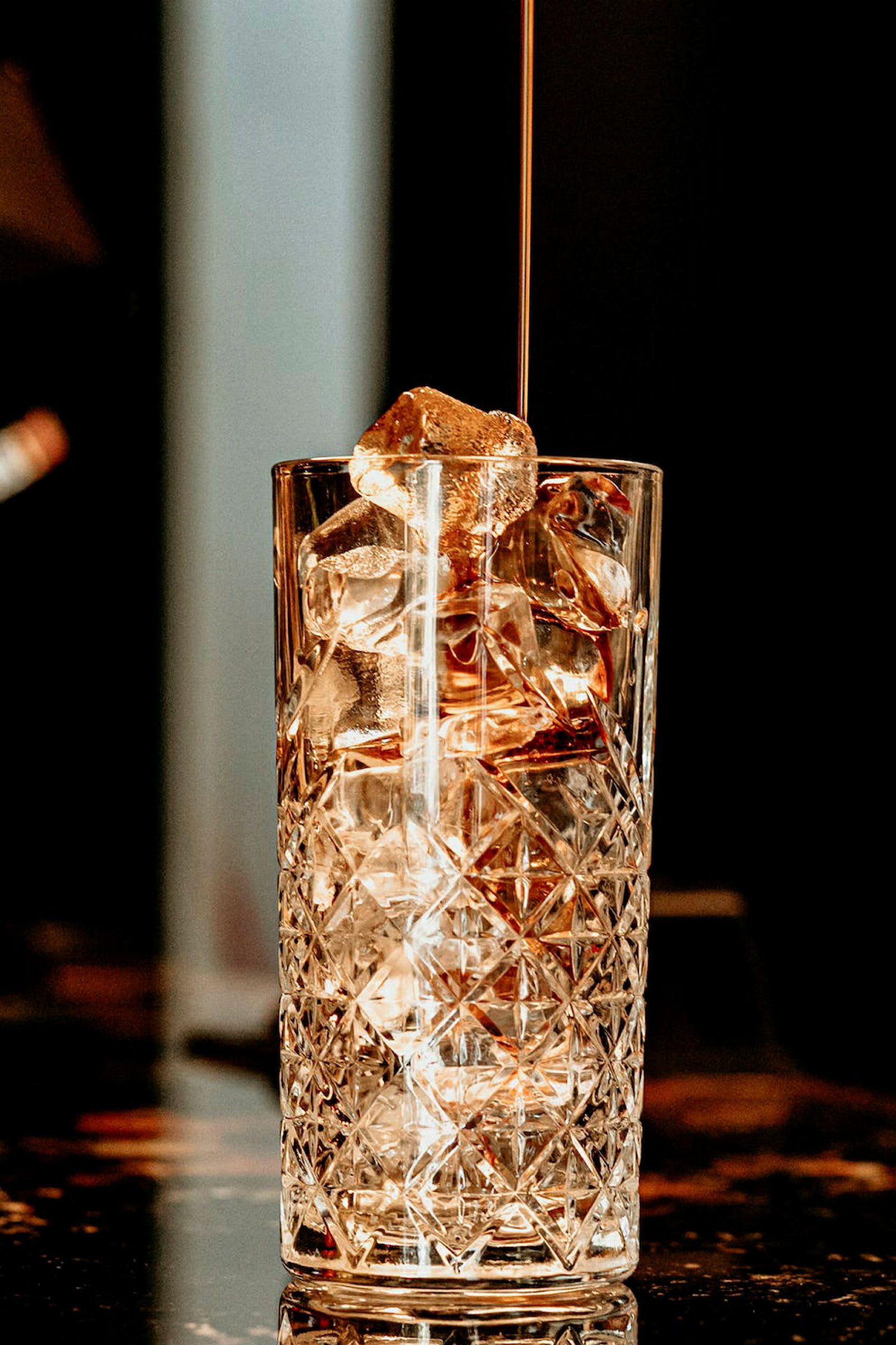 Et højt glas med isterninger og væske, der hældes i. (AI-genereret tekst)