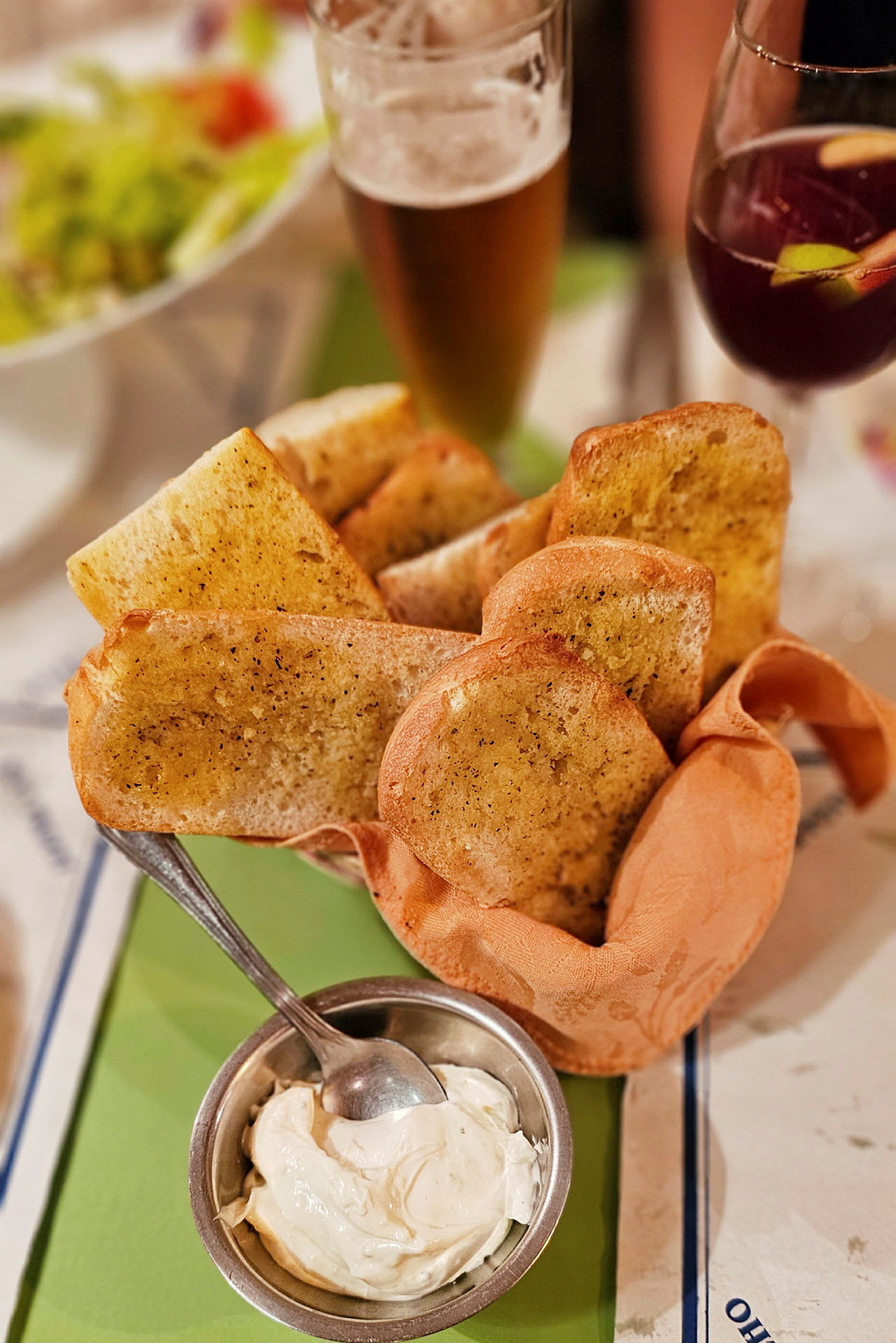 Hvidløgsbrød serveret med en skål med dip, samt glas med øl og sangria i baggrunden. (AI-genereret tekst)