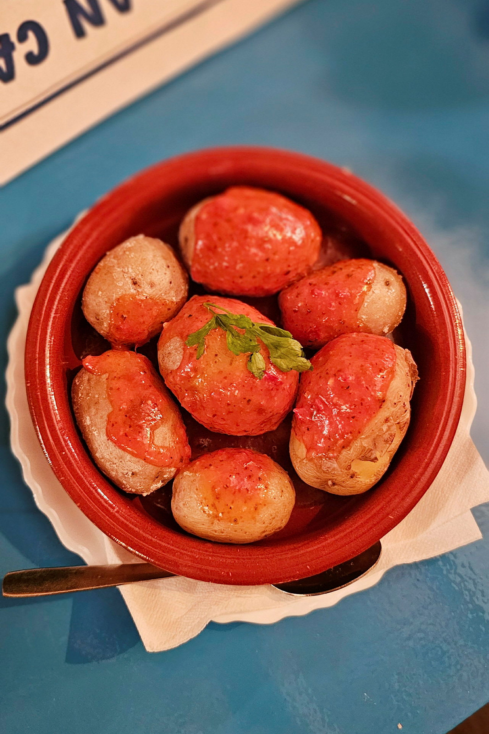 En skål med små kartofler dækket med rød sauce, pyntet med et grønt blad. (AI-genereret tekst)
