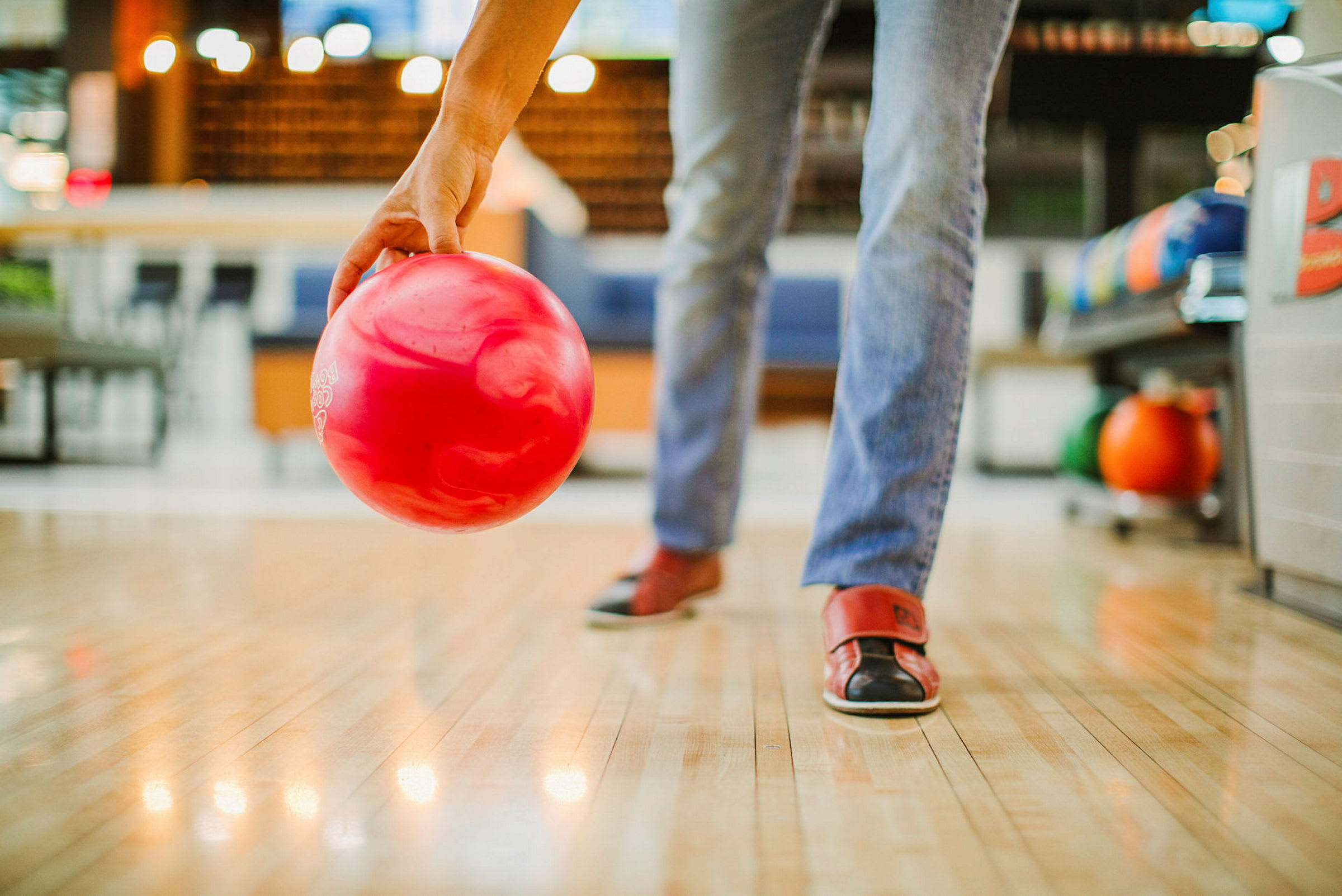 En person gør sig klar til at kaste en rød bowlingkugle på en bane. (AI-genereret tekst)
