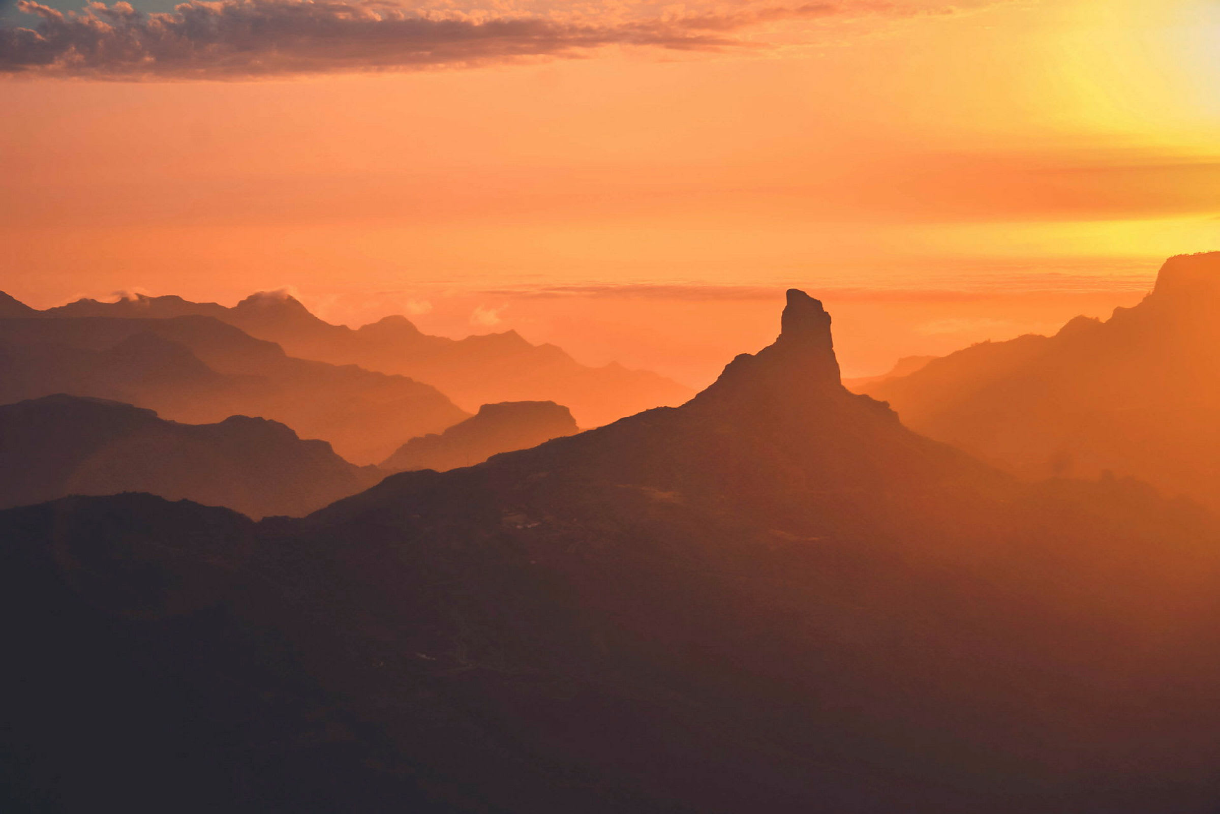 En bjergtop ses silhouetteret mod en orange og gul solnedgang. (AI-genereret tekst)