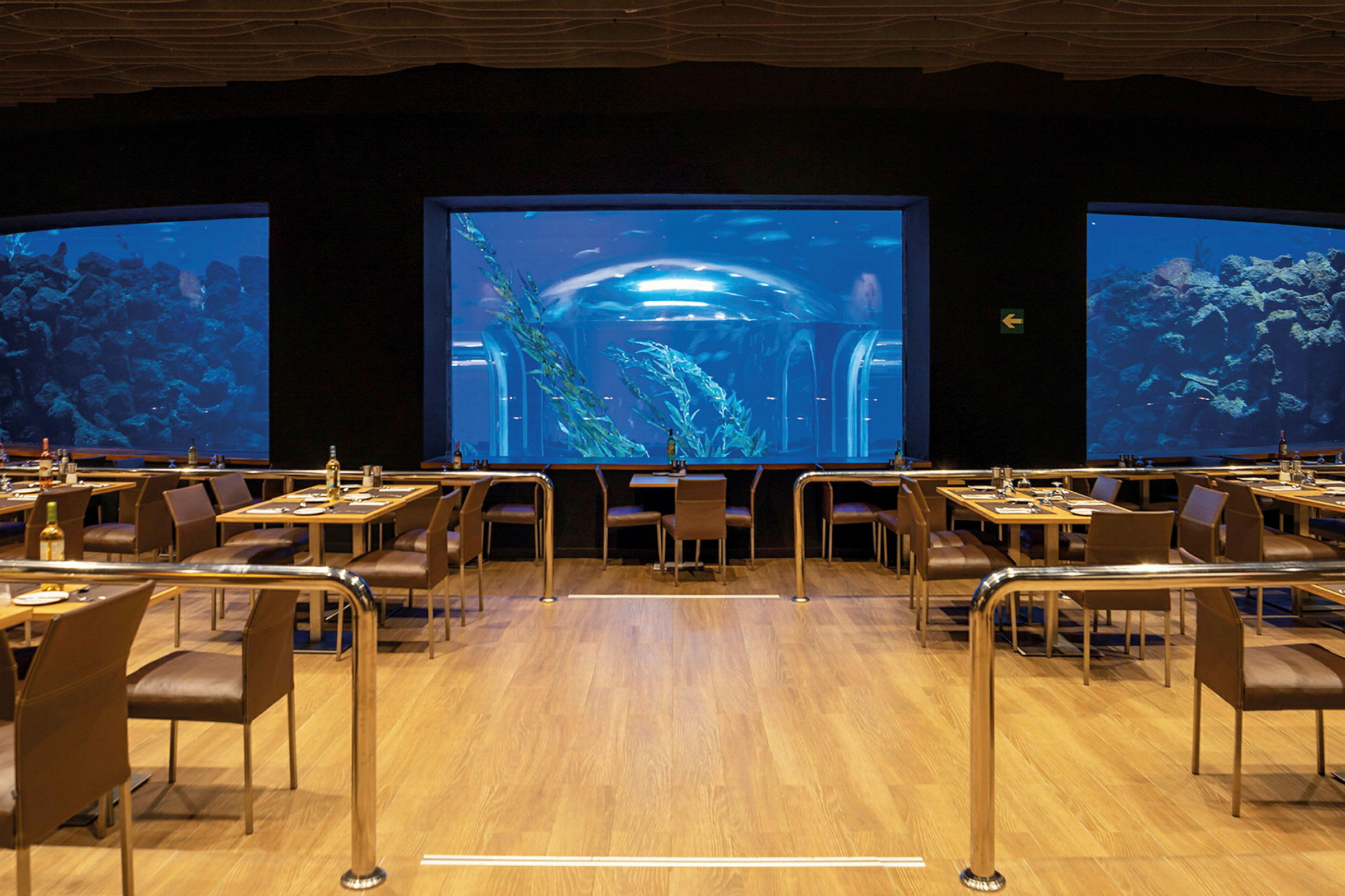 En restaurant med udsigt til et stort akvarium med fisk og undervandsmiljø. (AI-genereret tekst)