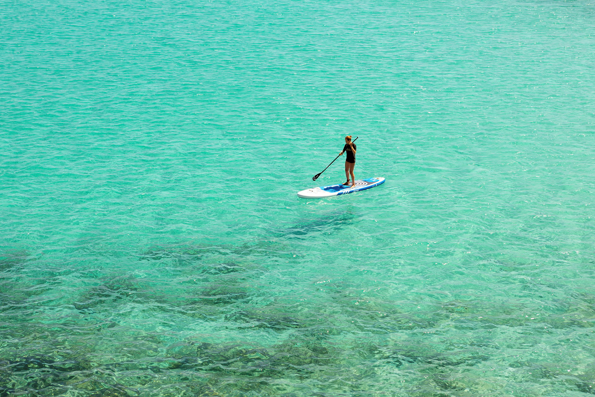 Person der padler stående på et paddleboard i klart turkisblåt vand. (AI-genereret tekst)