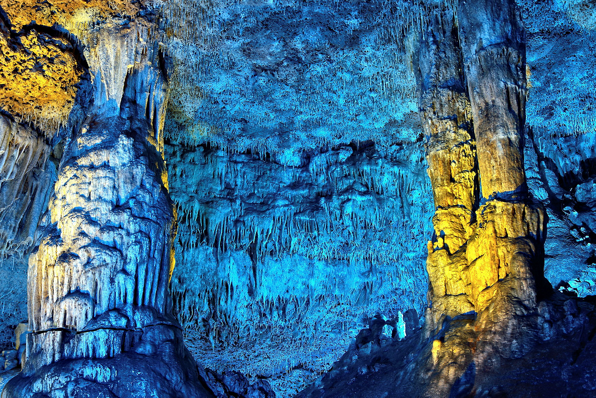 Et grottesystem med farverig belysning, der oplyser stalaktitter og stalagmitter. (AI-genereret tekst)