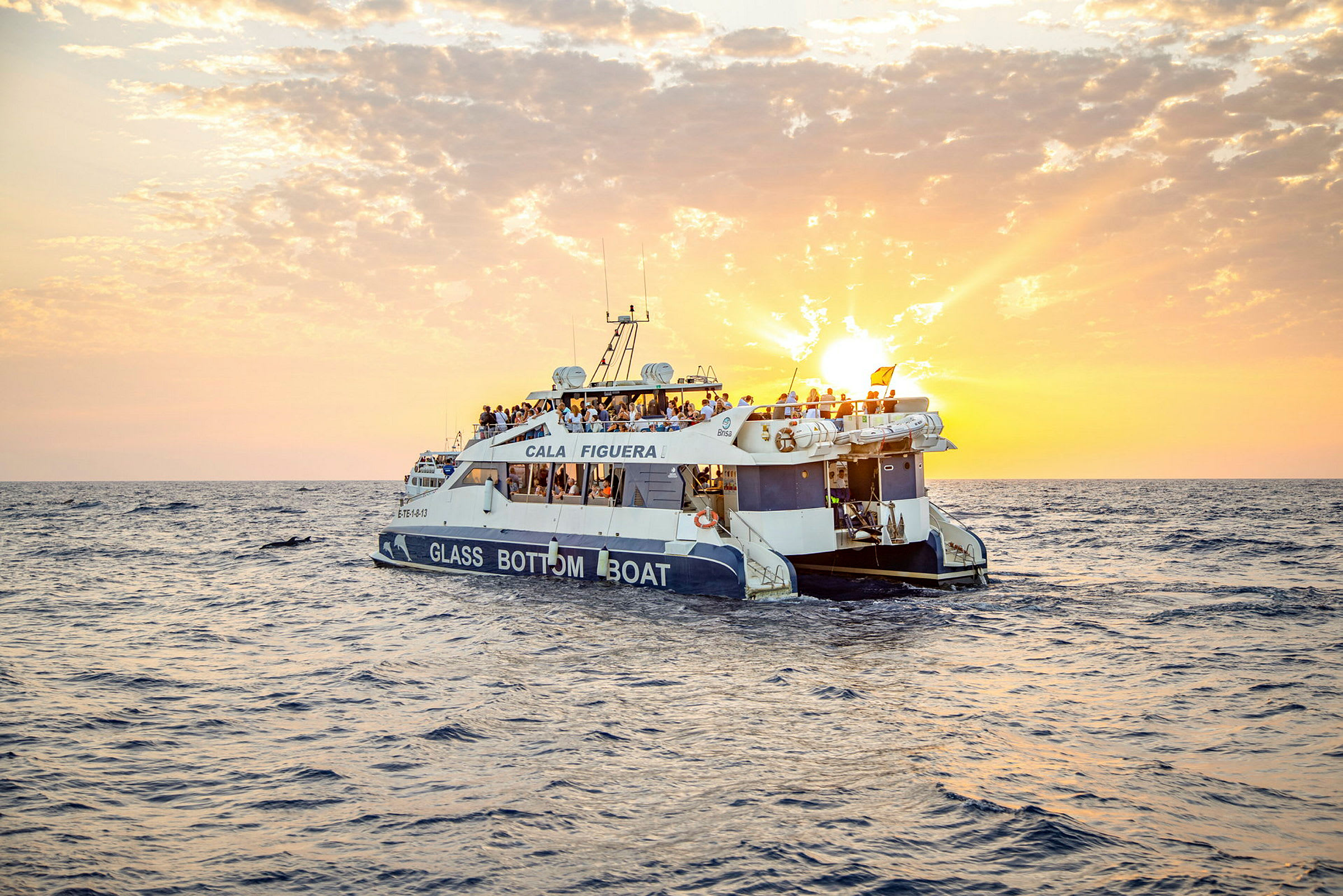 En glasbundsbåd med mennesker ombord sejler på havet under en solnedgang. (AI-genereret tekst)
