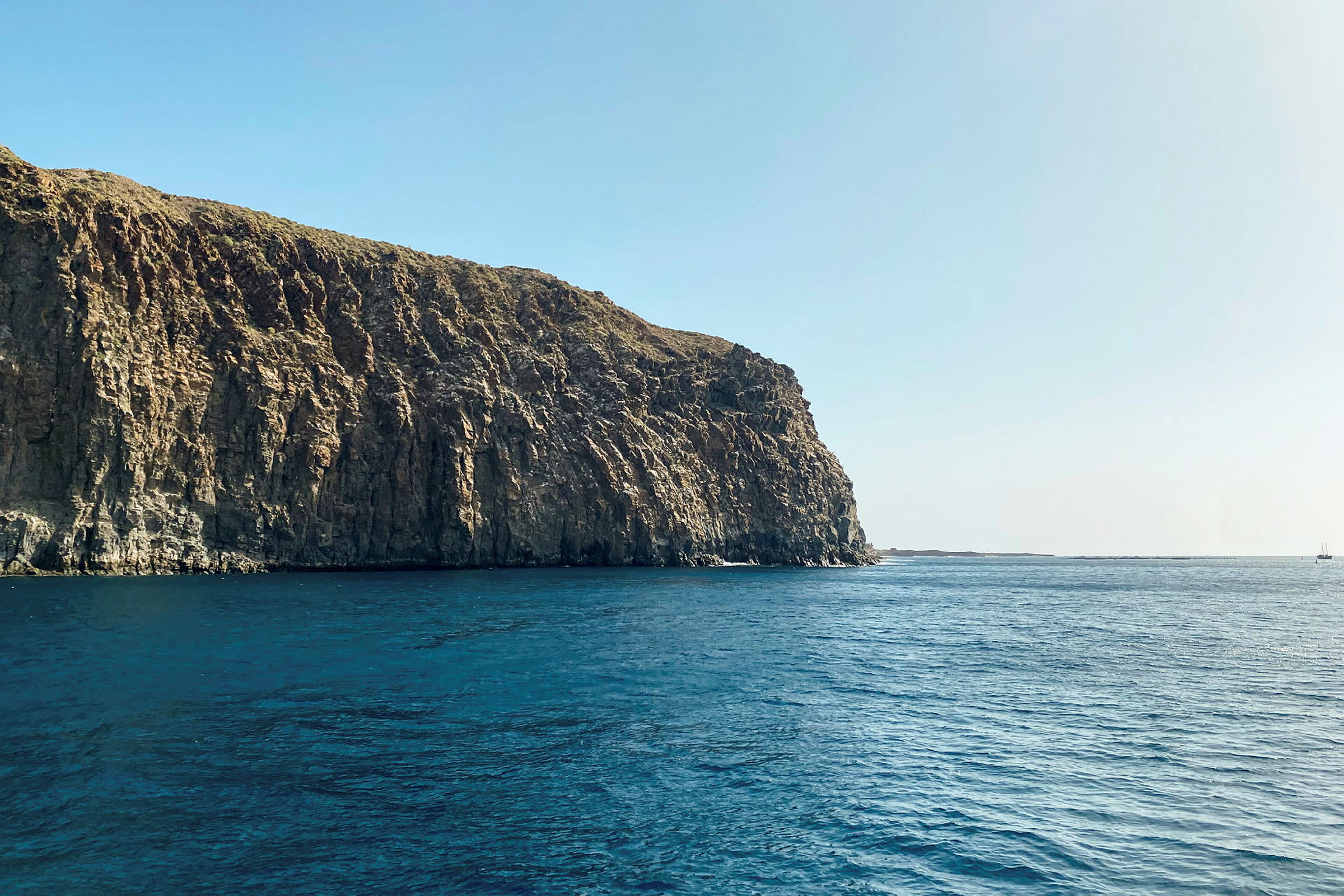 En høj klippe ved havet under en klar blå himmel. (AI-genereret tekst)