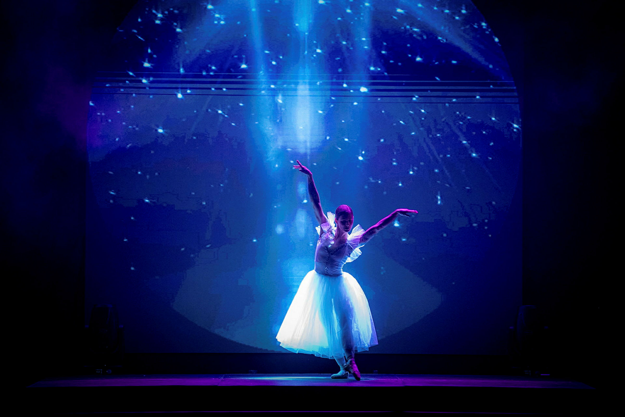 En balletdanser i hvid kjole poserer på en scene mod en stjernefyldt baggrund. (AI-genereret tekst)