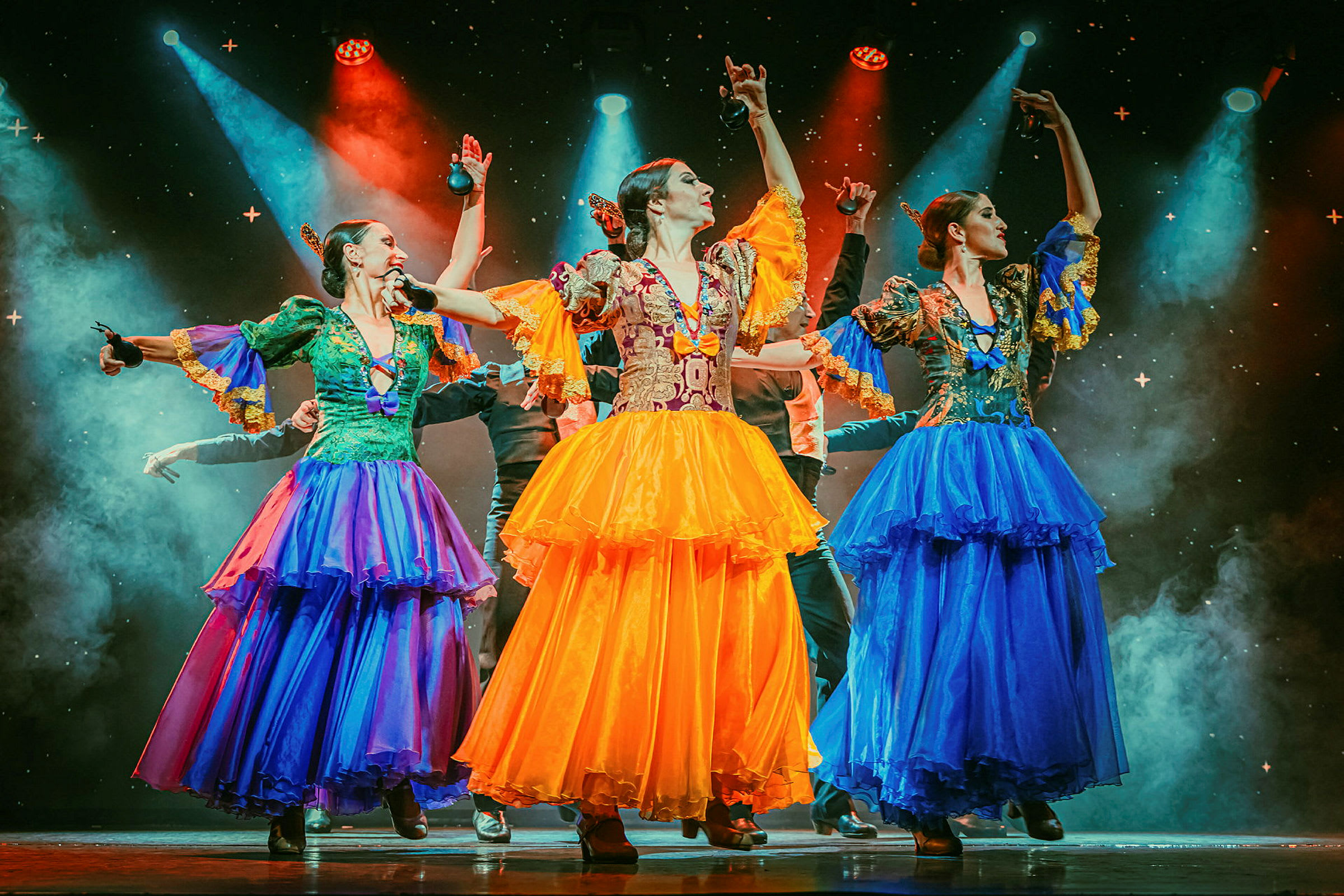 Tre personer iført farverige traditionelle dragter danser på en oplyst scene. (AI-genereret tekst)