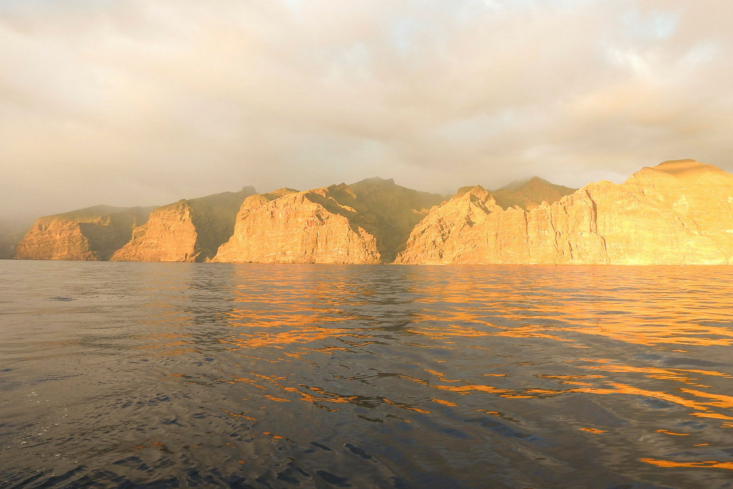 Solbelyste klipper ved havet under overskyet himmel. (AI-genereret tekst)