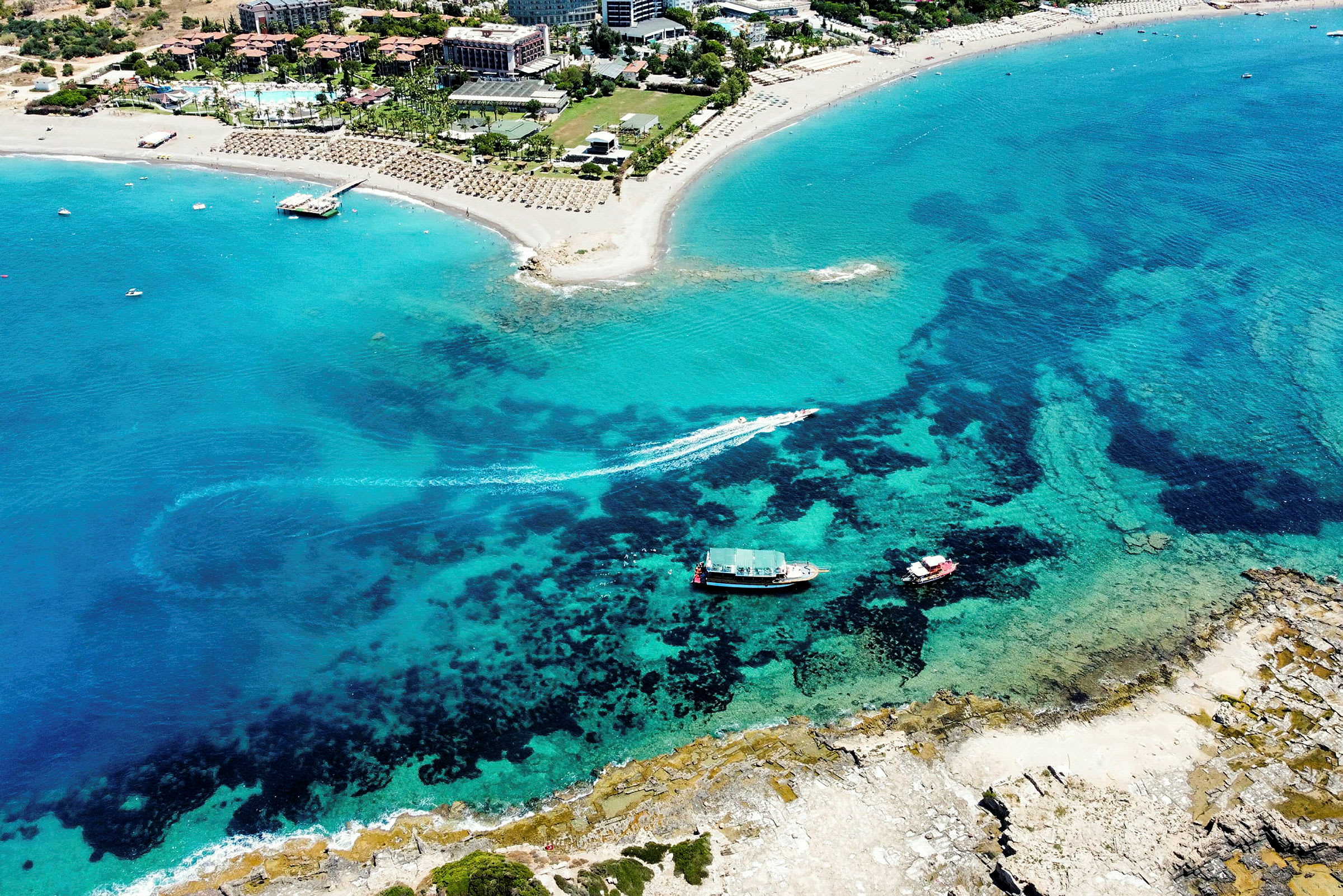 Luftfoto af en sandstrand ved et turistområde med klart blåt vand. (AI-genereret tekst)
