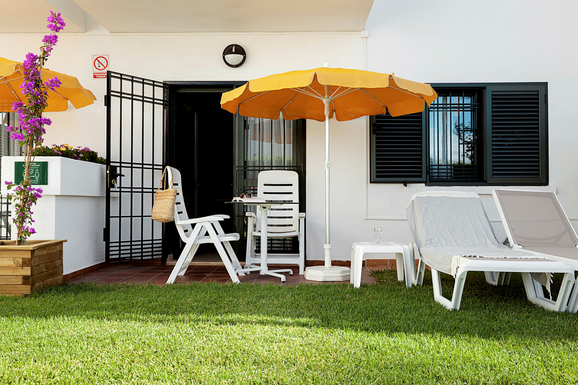 Terrasse med hvide plaststole, orange parasol og liggestole på græsplæne. (AI-genereret tekst)