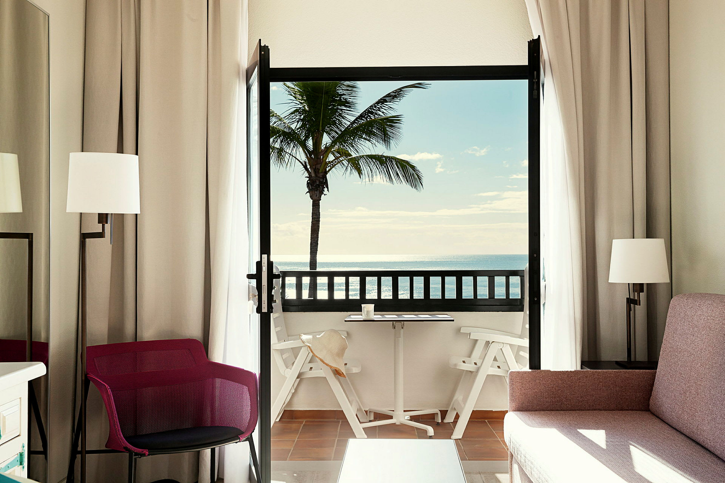 Et hotelværelse med balkon, der viser en palme og havudsigt. (AI-genereret tekst)